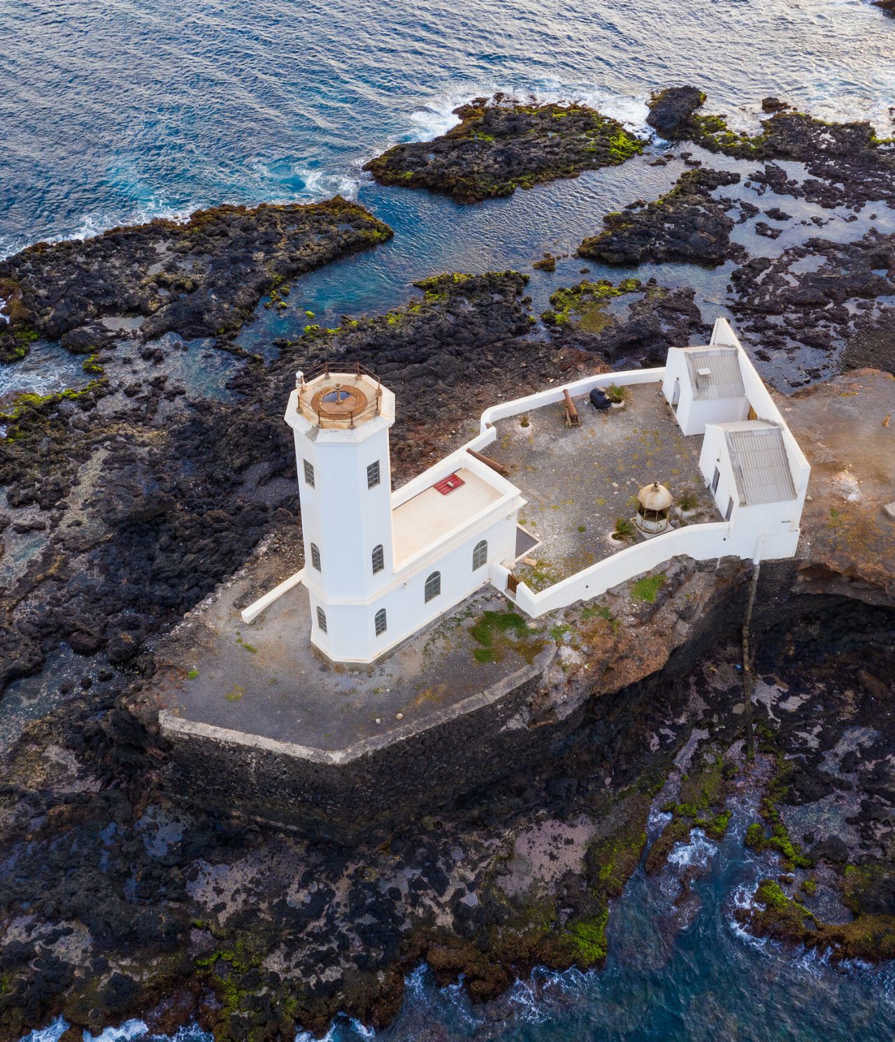 Vista aérea de un faro rodeado por el mar y rocas esculpidas por la naturaleza