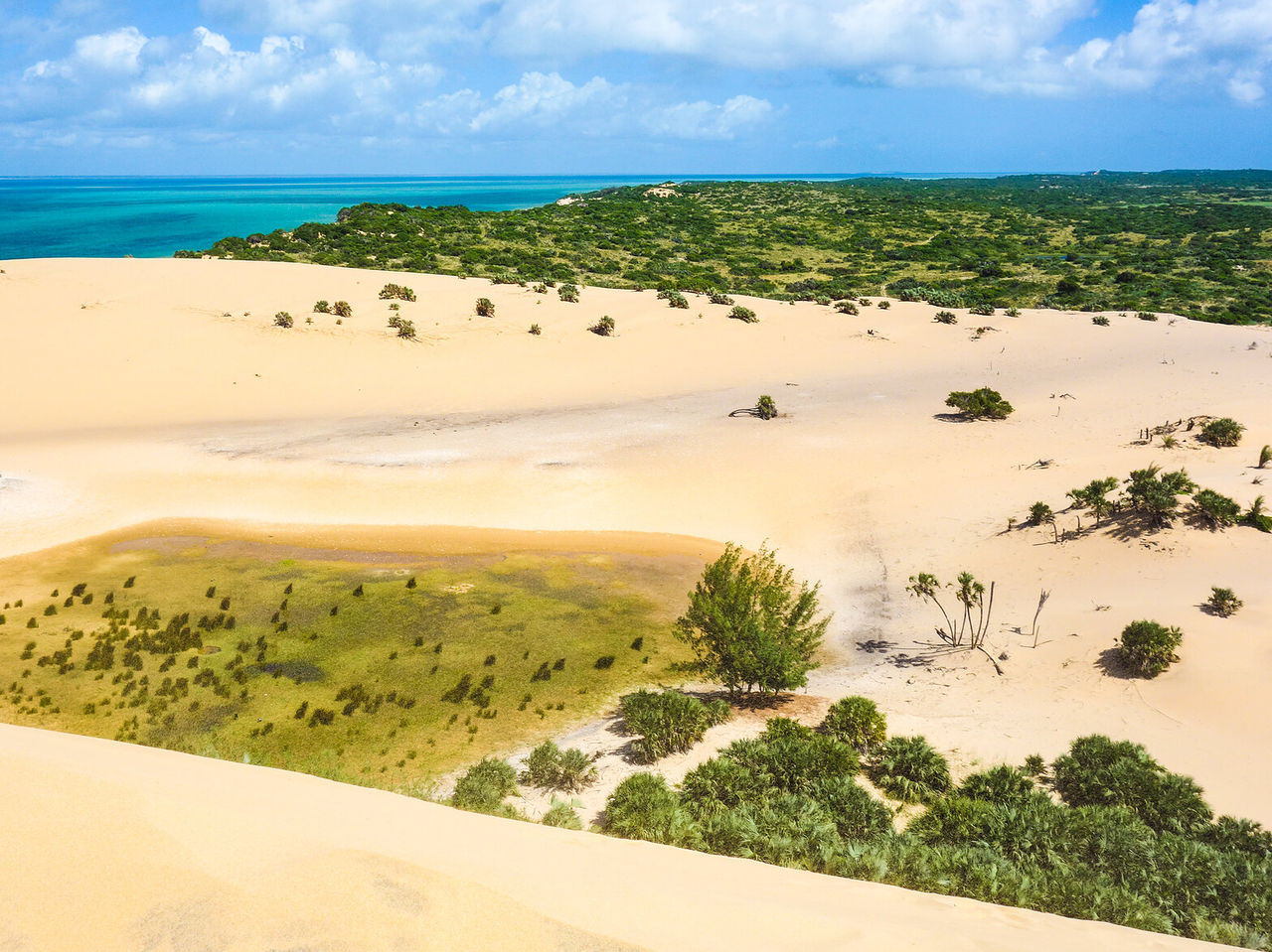 Vista aérea de un paisaje desértico con dunas de arena blanca en contraste con las aguas cristalinas del océano