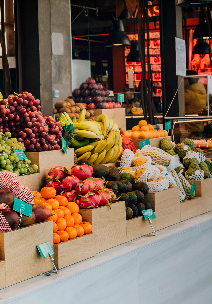 Puesto con frutas en el Mercado de San Miguel, con balanza y lámparas de techo negras, y un mostrador de vidrio