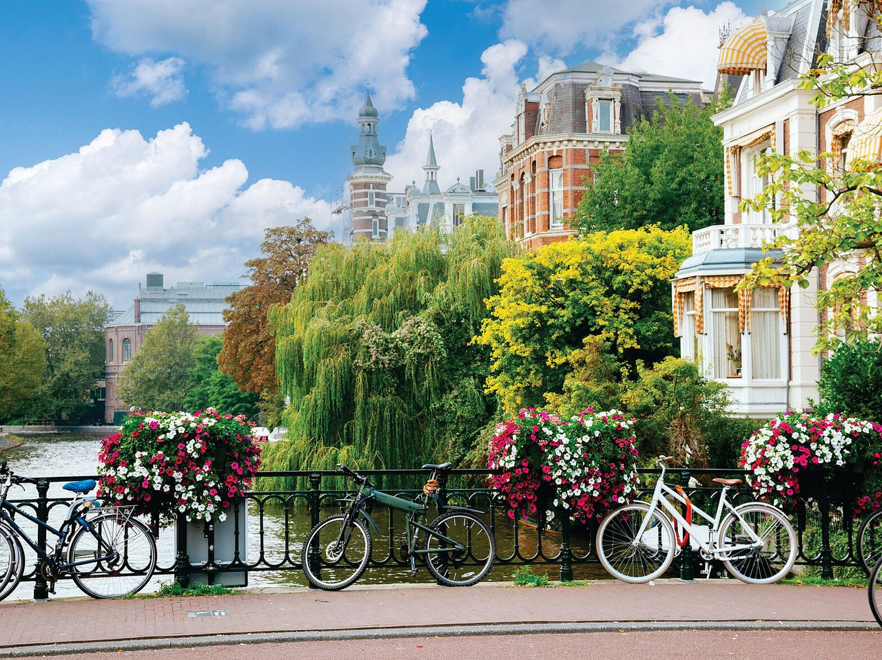 Puente sobre un canal en Ámsterdam, con bicicletas estacionadas, flores coloridas y edificios típicos de fondo
