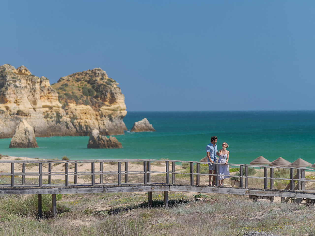 Casal a admirar a vista de uma praia no Alvor, no Algarve, enquanto passeiam pelos passadiços à beira mar