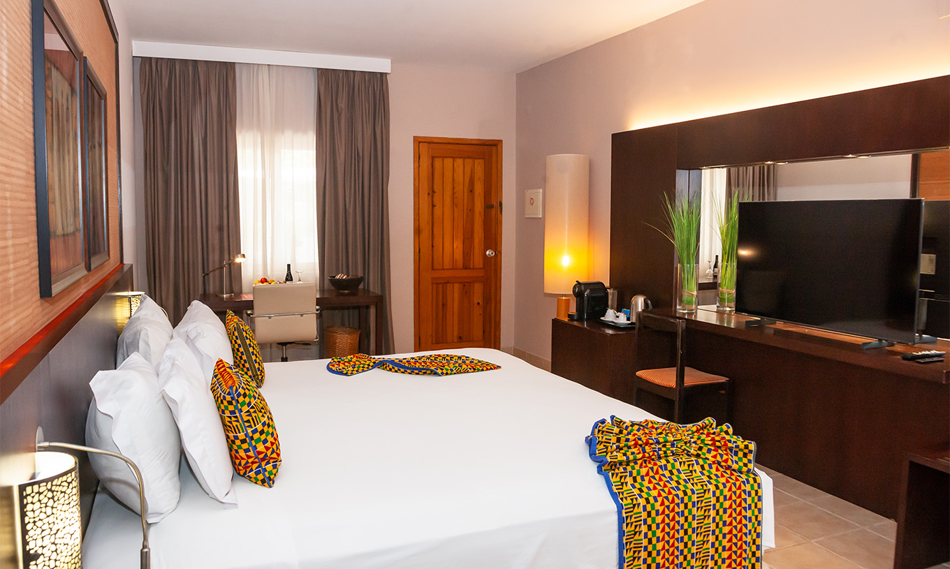 Junior Suite Pestana Tropico hat ein Doppelbett, Fernseher, Spiegel und Schreibtisch mit Stuhl und Obstkorb