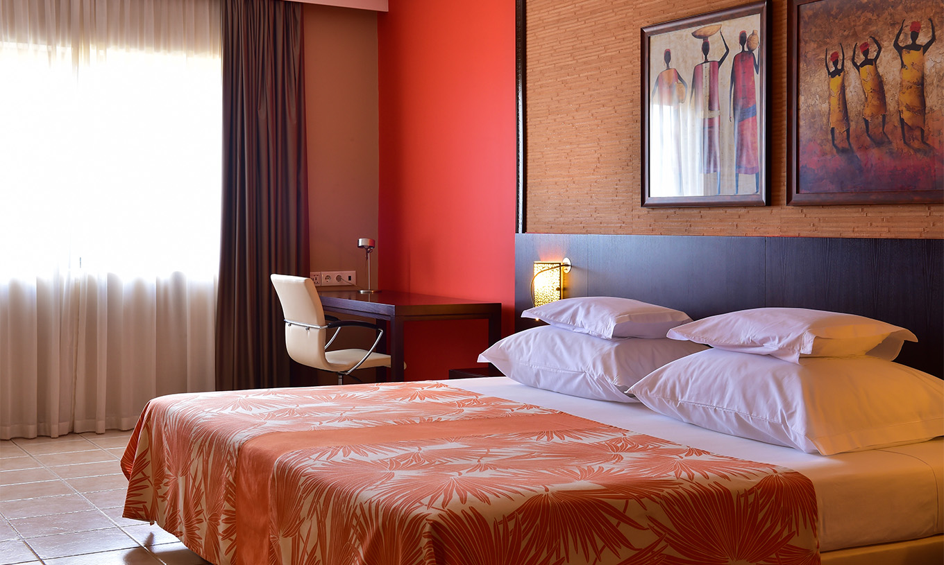 Standardzimmer Pestana Tropico hat ein Doppelbett, Schreibtisch mit Stuhl und Nachttisch mit Lampe