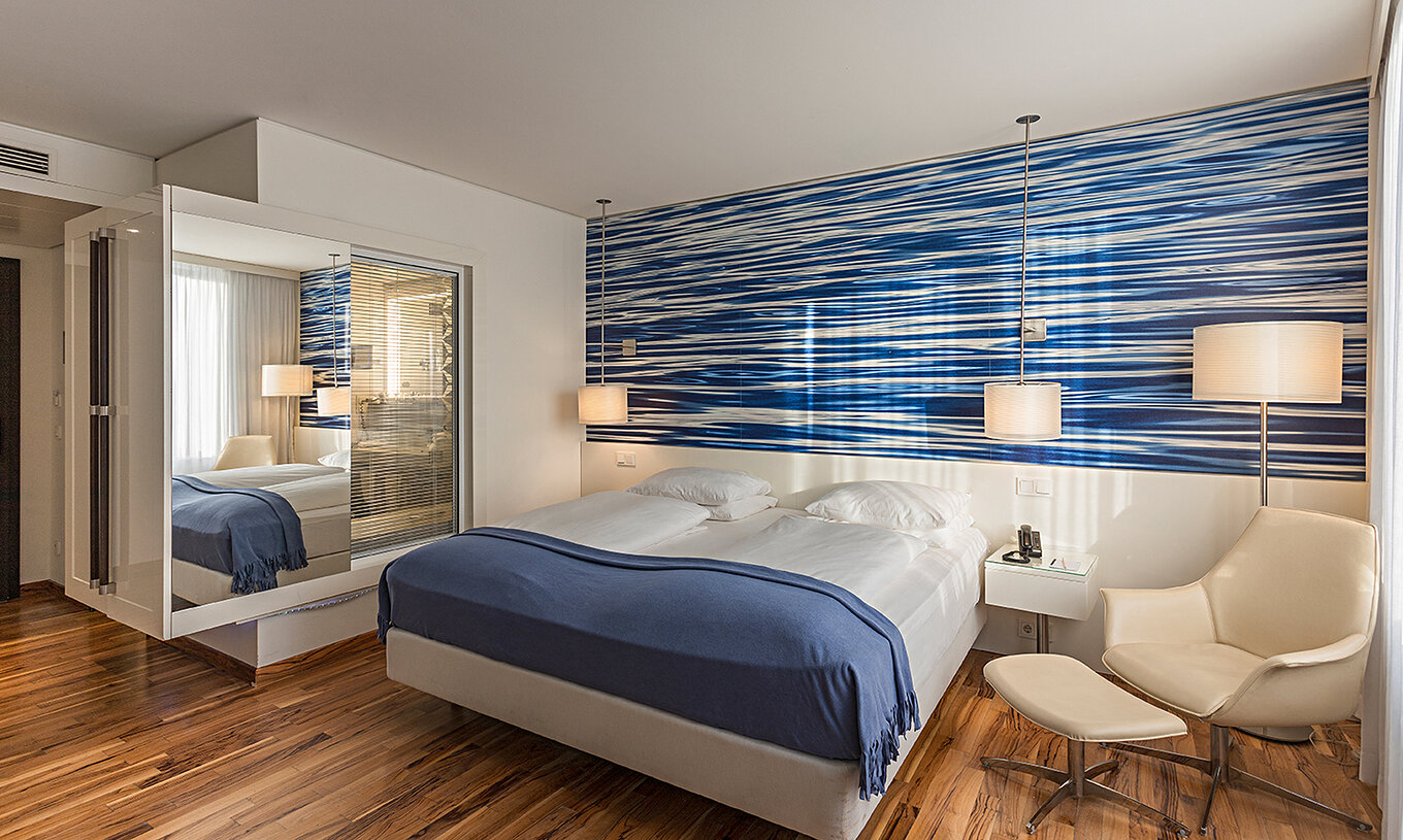 Das Deluxe Zimmer im Pestana Berlin Tiergarten hat ein Doppelbett, Nachttisch mit Telefon und ein Sofa