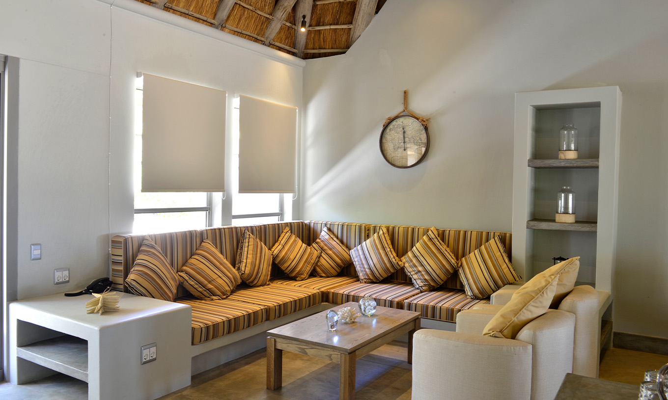 Die T2 Villen im Pestana Bazaruto Lodge haben ein L-förmiges Sofa aus Stein mit bunten Kissen und zwei Sesseln