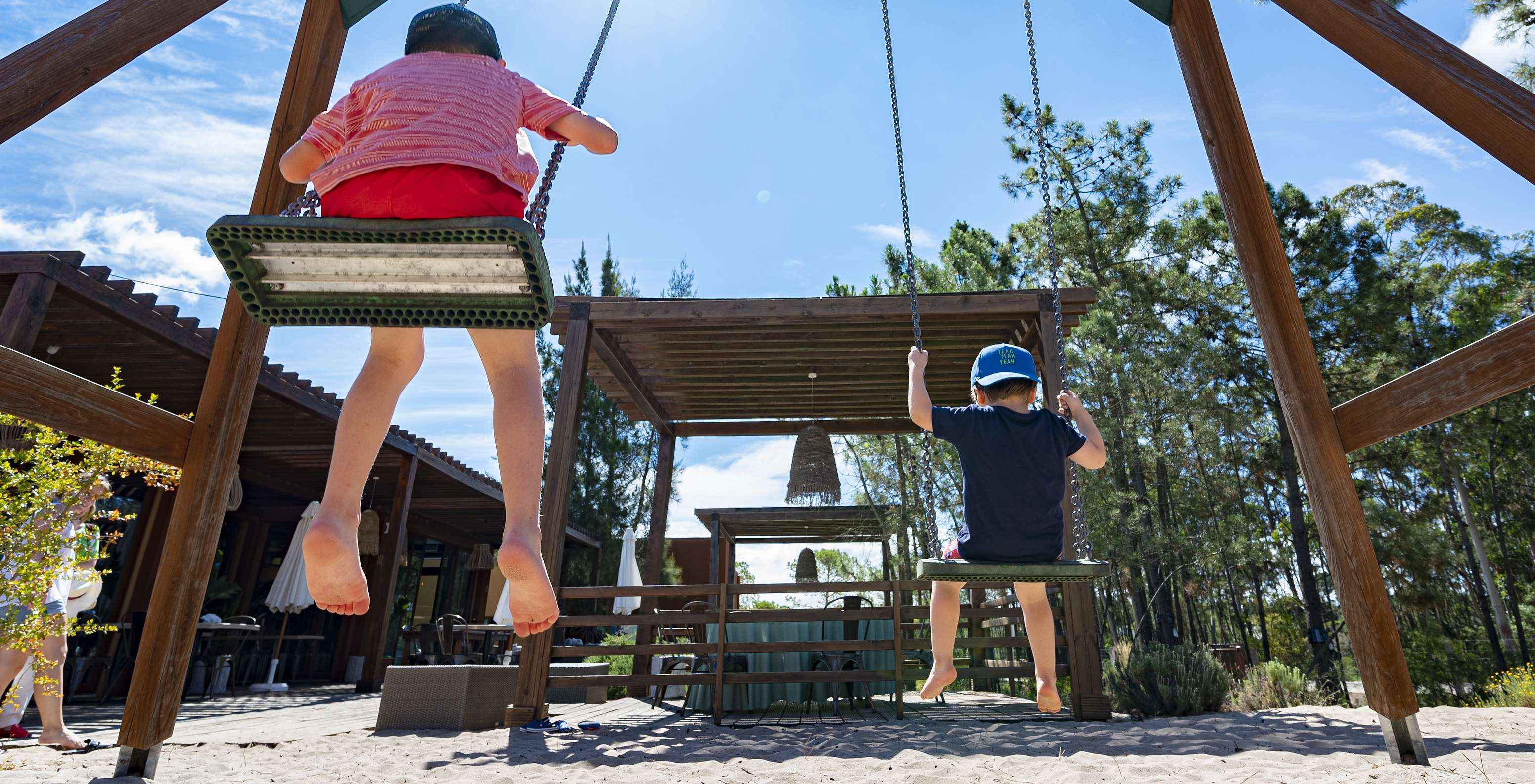 Schaukeln mit zwei Kindern auf einem kleinen Spielplatz neben dem Restaurant des Pestana Tróia Eco Resort