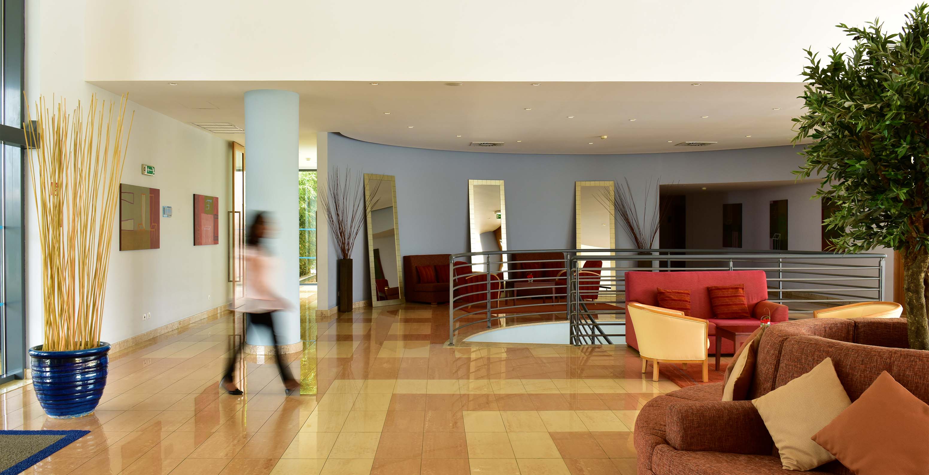 Eingang des Hotels mit roten und orangefarbenen Sofas, mit Metalltreppen und einer Dame, die geht