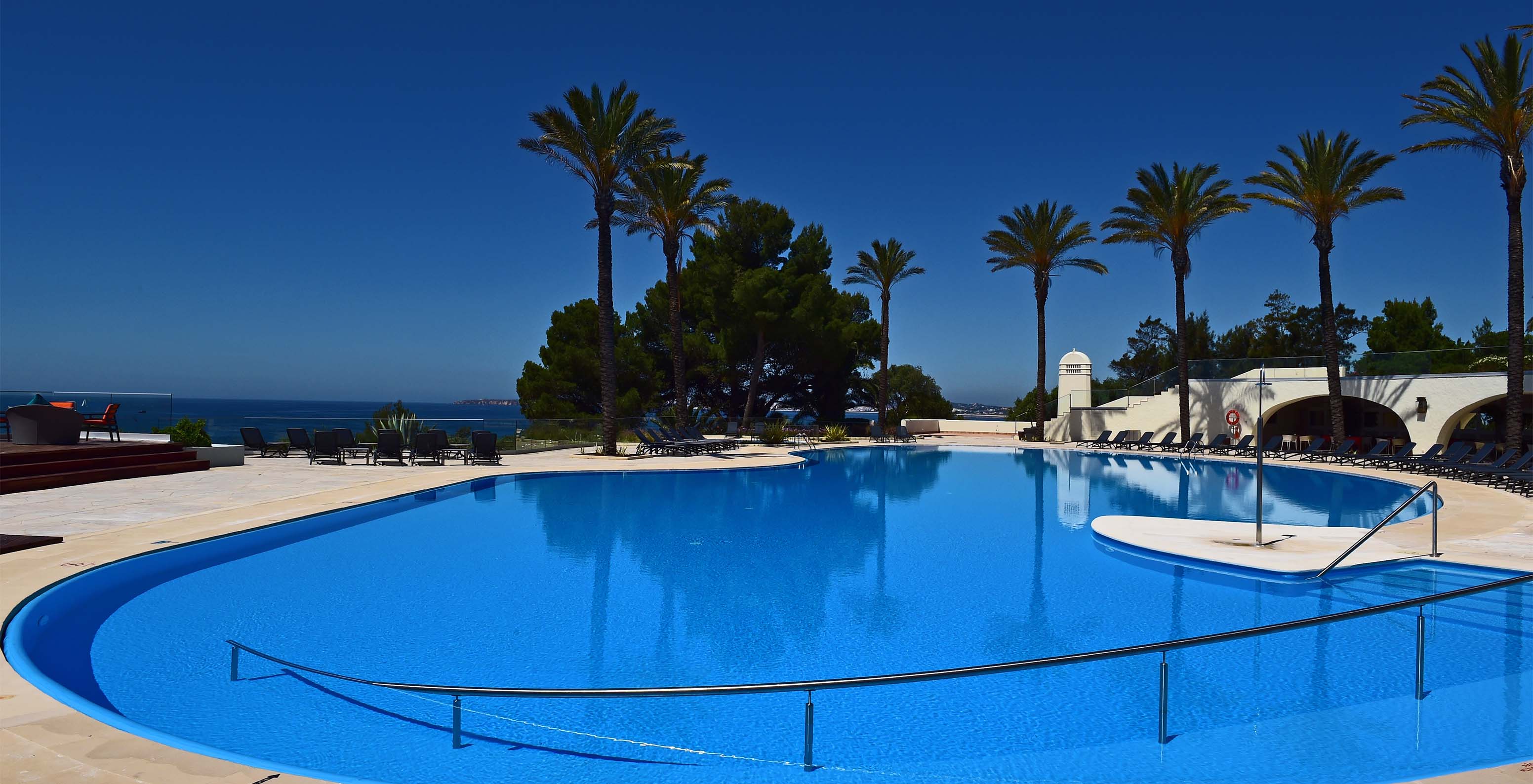 Außenpool mit Liegen, Palmen und Terrasse, Jacuzzi, Blick auf das Meer und den Strand, und wolkenlosem Himmel