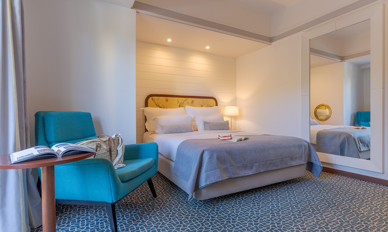 Das Deluxe im Pestana Alvor Praia hat ein Doppelbett, einen Tisch mit einem blauen Sessel und einen Spiegel