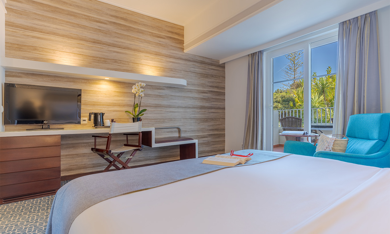 Das Deluxe im Pestana Alvor Praia hat ein Doppelbett, Fernseher am Schreibtisch, blauen Sessel und Fenster