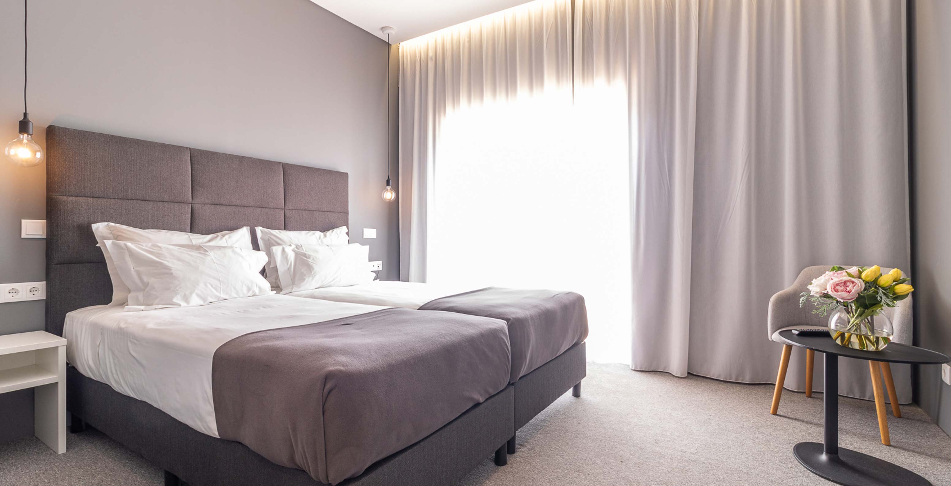 Klassisches Zimmer im Pestana Gramacho Residences mit zwei Betten, Vorhängen und Tisch mit Blumen