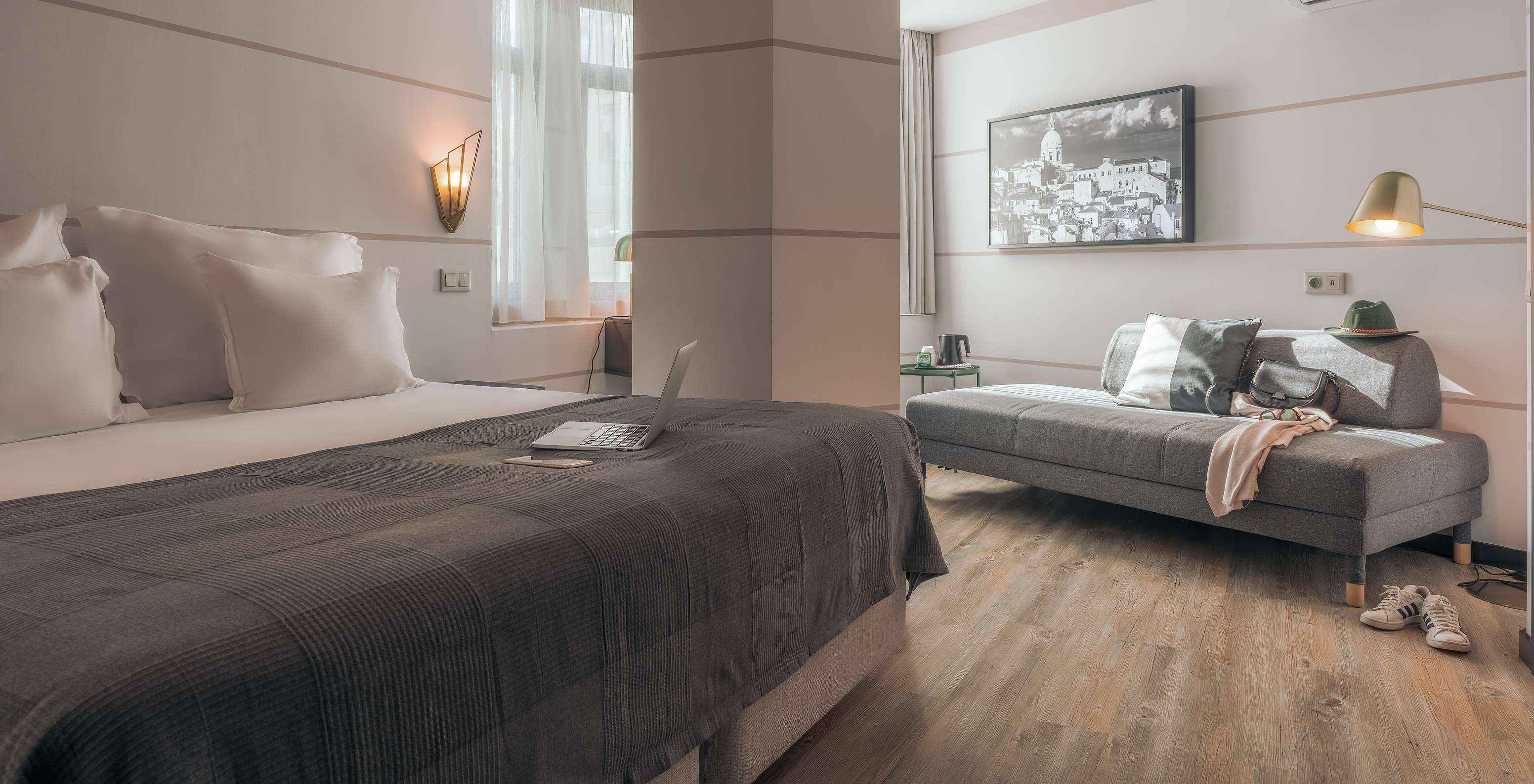 Das Double Superior im Pestana Lisboa Vintage hat Doppelbett mit grauer Decke, graues Sofa und weiße Sneakers