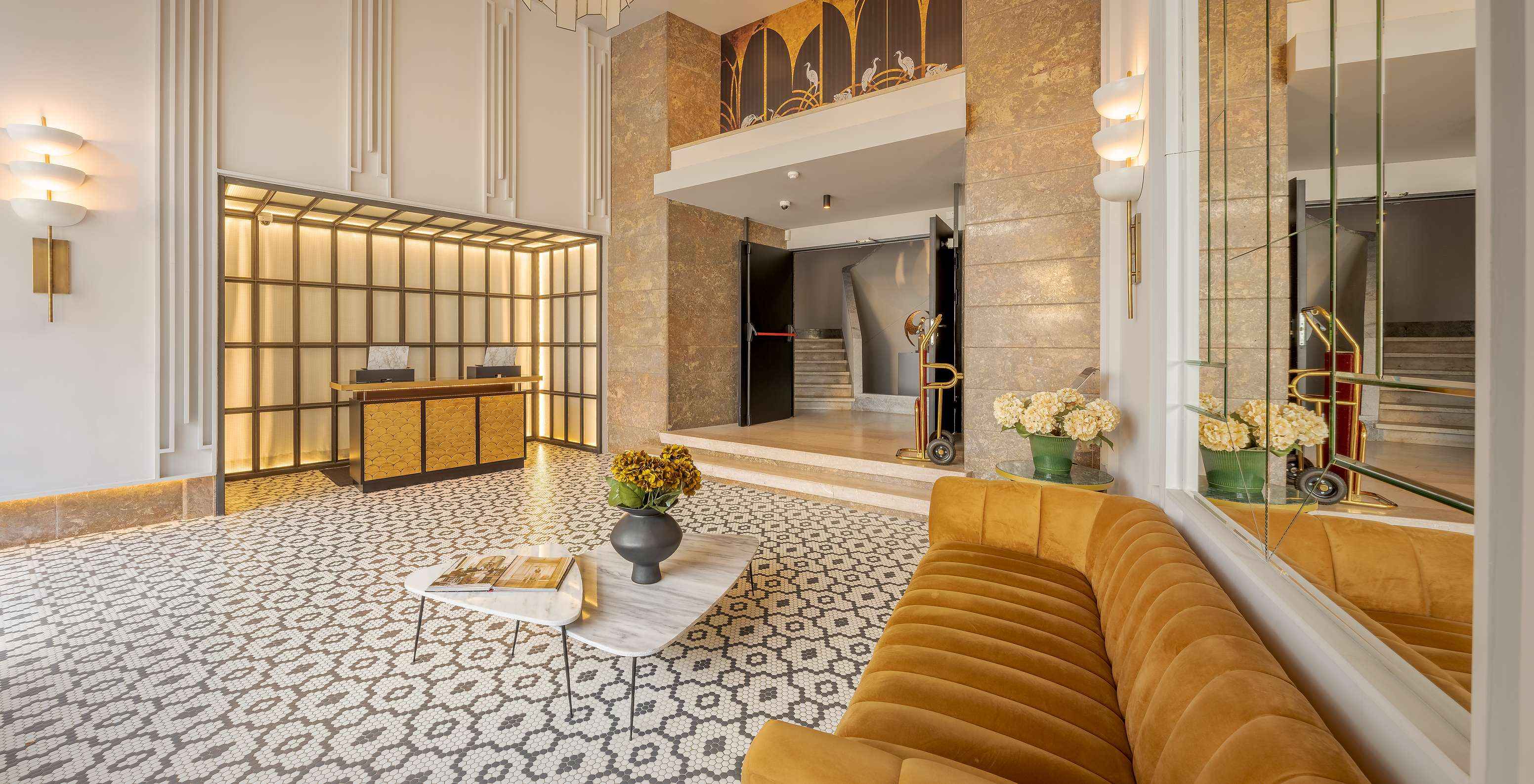 Lounge der Rezeption mit einem Paar und einem Kind, Spiegeln, einem Sofa, Beistelltischen mit Blumenvasen und Empfang