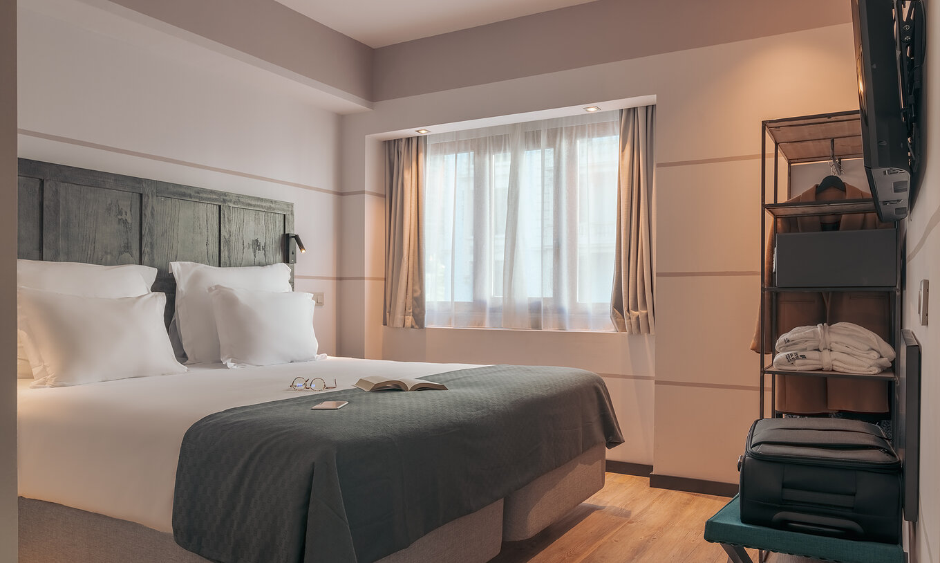 Das Double Deluxe Studio im Pestana Lisboa Vintage hat Doppelbett mit grauer Decke und Schrank mit Jacke