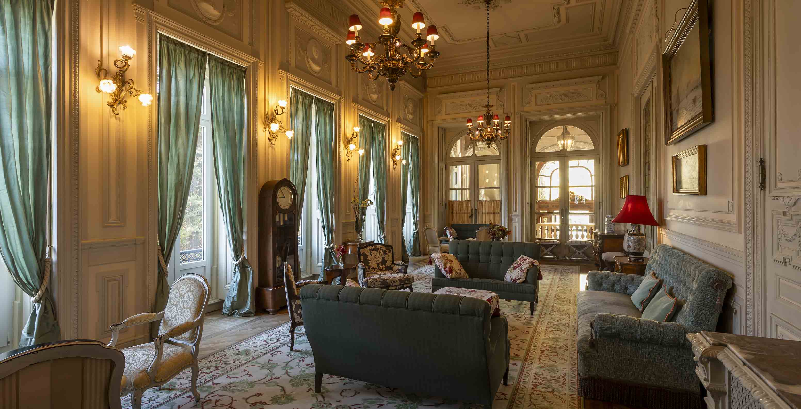 Das Pestana Palace Lisboa hat einen Lounge-Bereich im Palast mit Sofas, Sesseln und langen grünen Vorhängen an den Fenstern