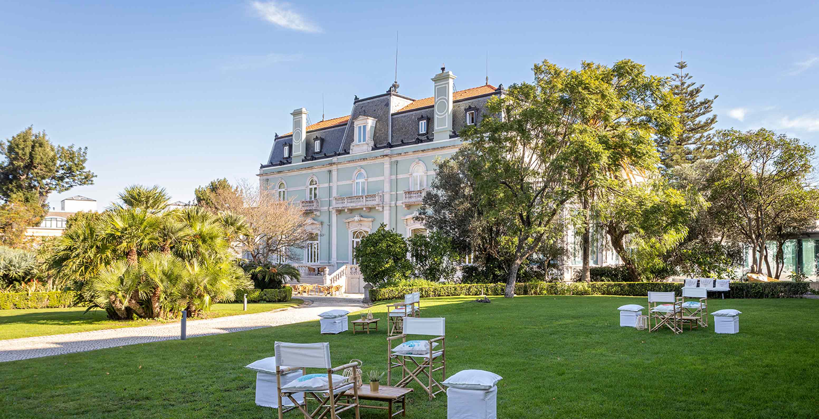 Das Pestana Palace Lisboa hat einen Garten mit Tischen und Stühlen auf grünem Rasen, nahe dem Hauptgebäude	