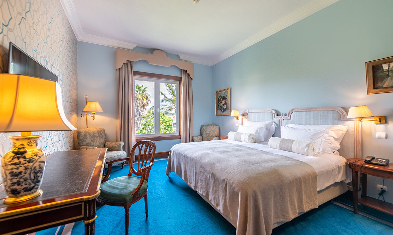 Das Premium Garden Zimmer im Pestana Palace Lisboa hat ein Doppelbett, Nachttische und ein Fenster mit Gartenblick
