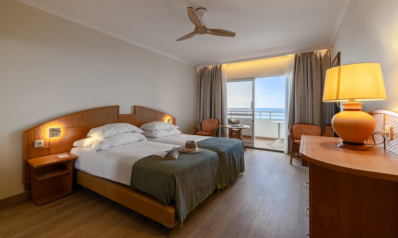 Das Classic Sea View im Pestana Ocean Bay All Inclusive verfügt über ein Doppelbett zwei Stühle und einen Balkon mit Aussicht