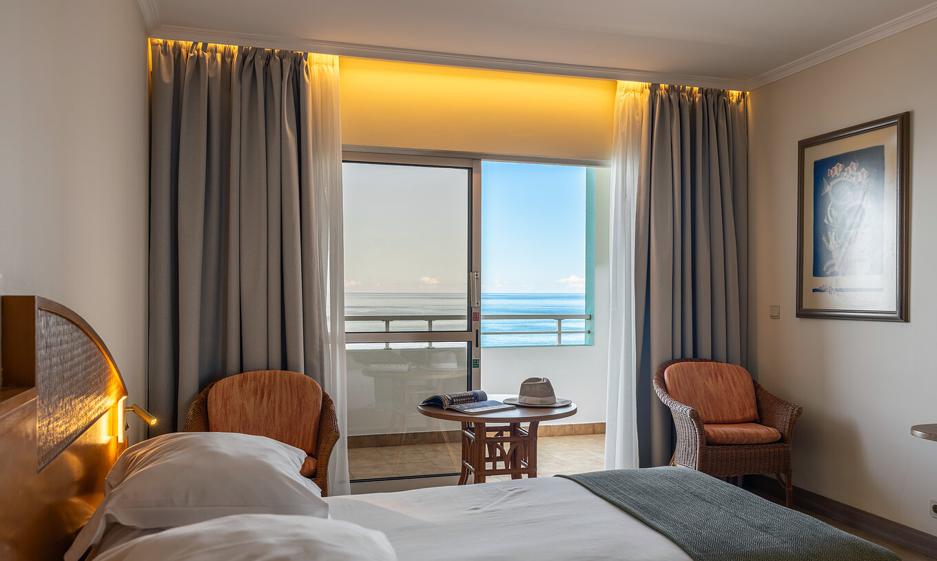Das Classic Sea View im Pestana Ocean Bay All Inclusive verfügt über ein Doppelbett zwei Stühle und einen Balkon mit Aussicht