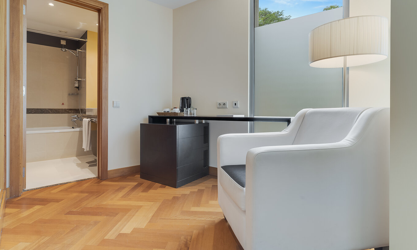 Das Twin Klassik Zimmer hat ein Bad mit Badewanne und einen Sessel und Tisch vor der Tür 