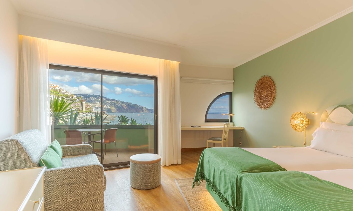 Das Superior seitlicher Meerblick im Pestana Vila Lido Madeira verfügt über ein großes Fenster, das auf den Balkon führt, einen Schreibtisch und ein Sofa