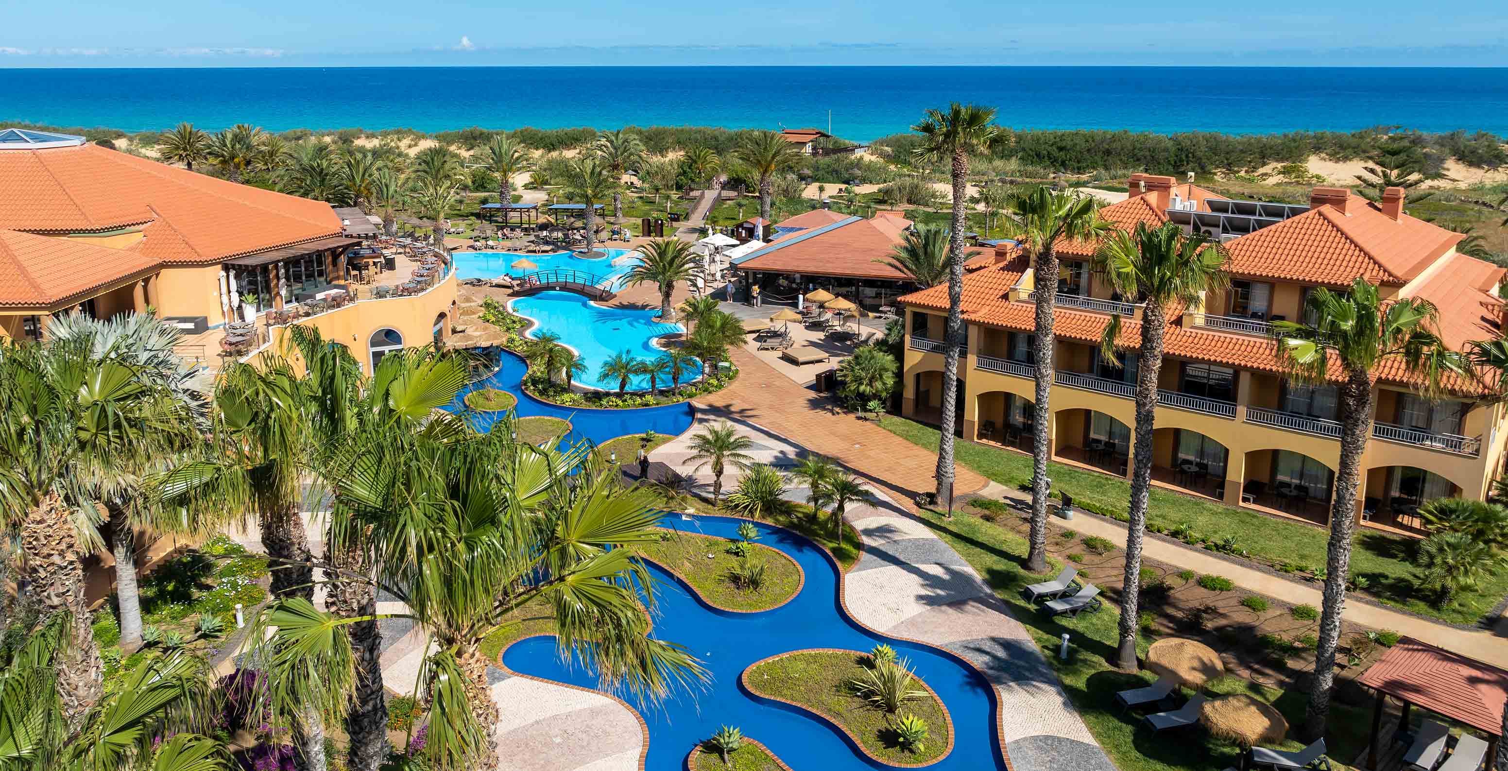 Blauer Außenpool des Pestana Porto Santo All Inclusive, umgeben von Palmen, Villen und Gärten