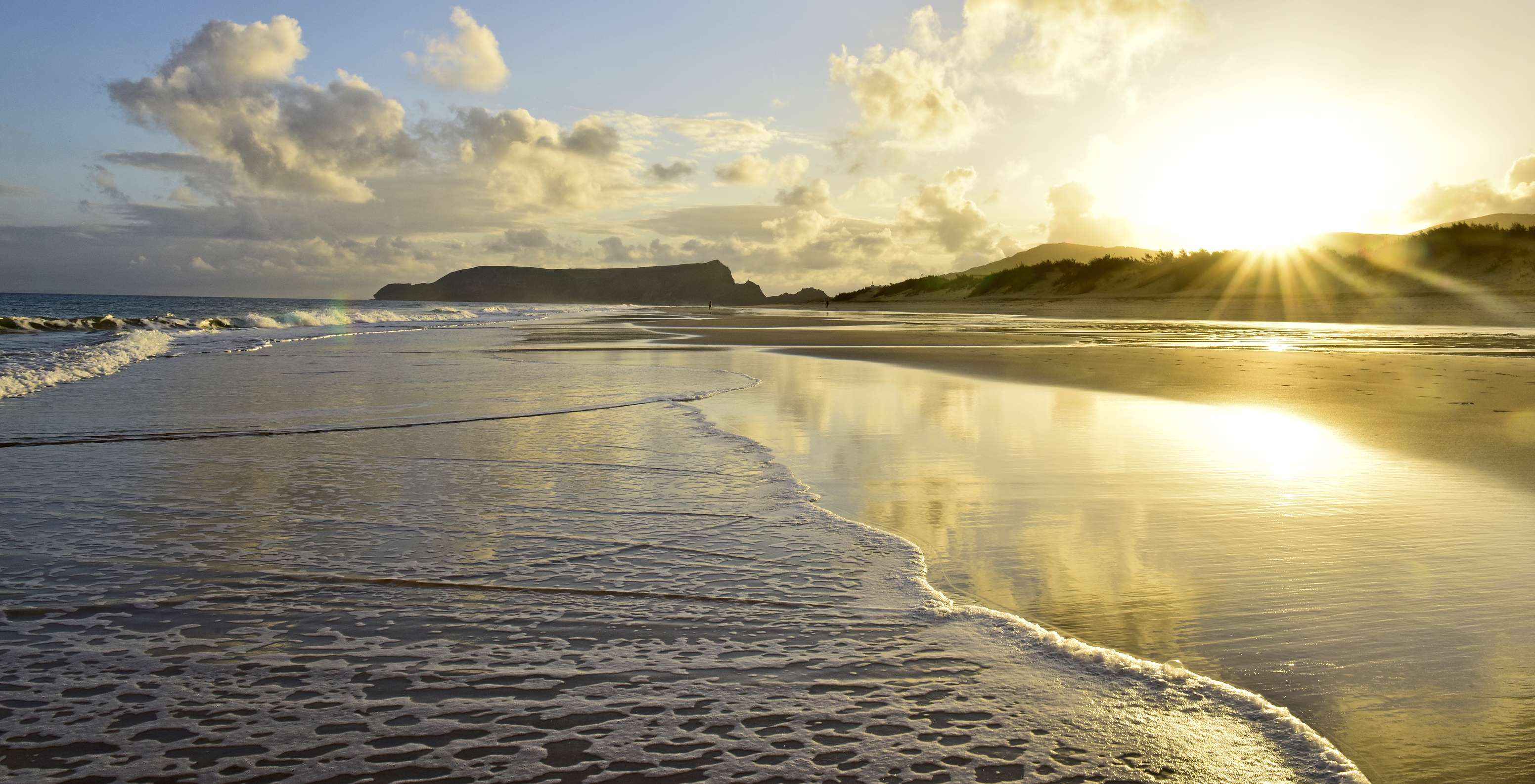 Sonnenuntergang am Strand von Porto Santo mit orangefarbenen Wolken und goldenen Strahlen