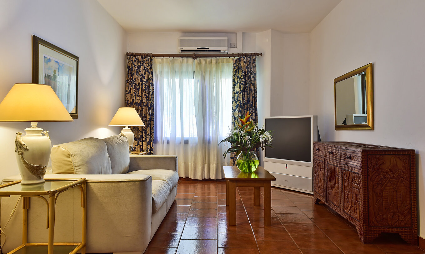 Die Suite im Pestana Miramar São Tomé hat ein Wohnzimmer mit Sofa, Fernseher und Tisch mit Blumenvase