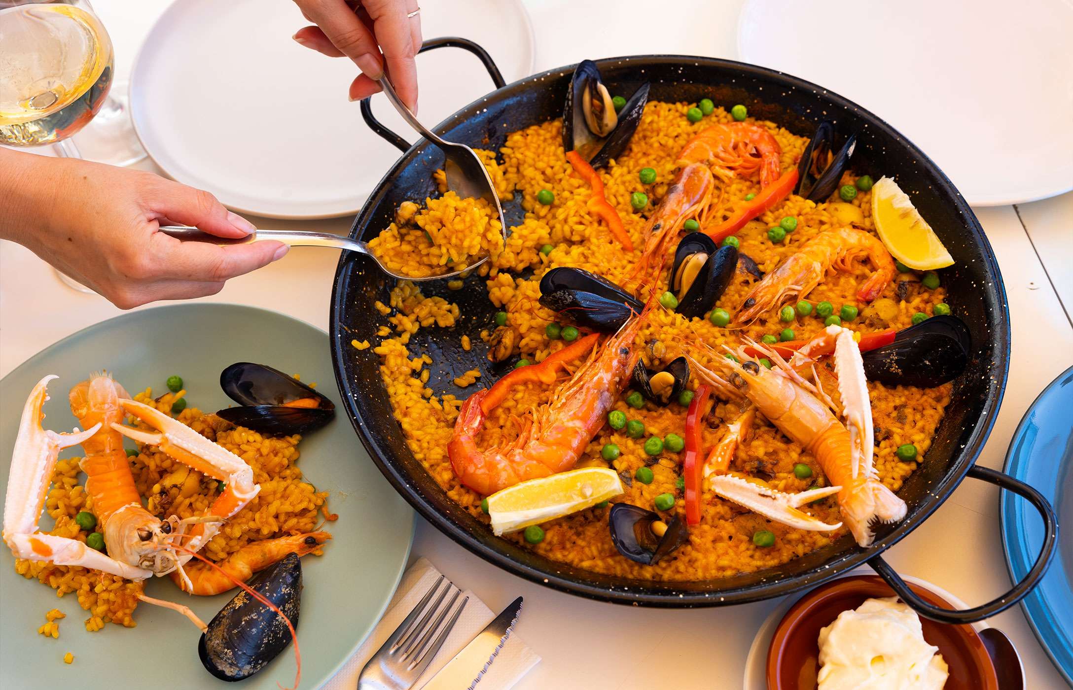 Person, die das typische spanische Gericht serviert, eine Paella-Pfanne, zubereitet mit Muscheln, Garnelen, Erbsen und Reis