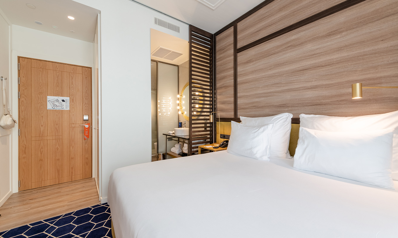 Das Premium Zimmer mit Balkon im Pestana CR7 Gran Vía Madrid hat ein Doppelbett und eine Holztrennwand mit Spiegel