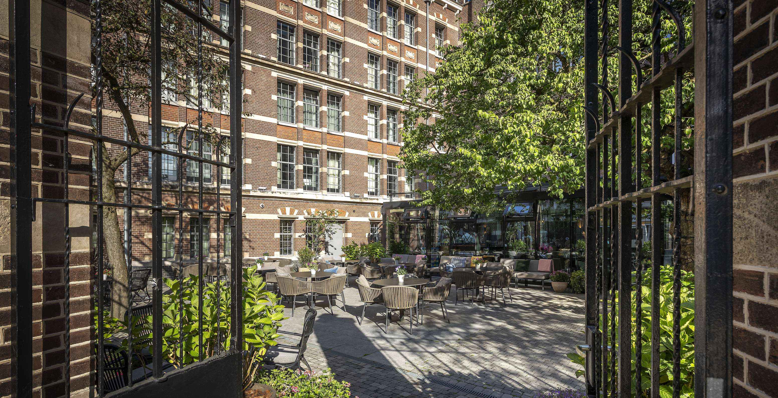 Terrasse des Pestana Amsterdam Riverside, mit runden Tischen und Stühlen, mit der Hotelfassade im Hintergrund