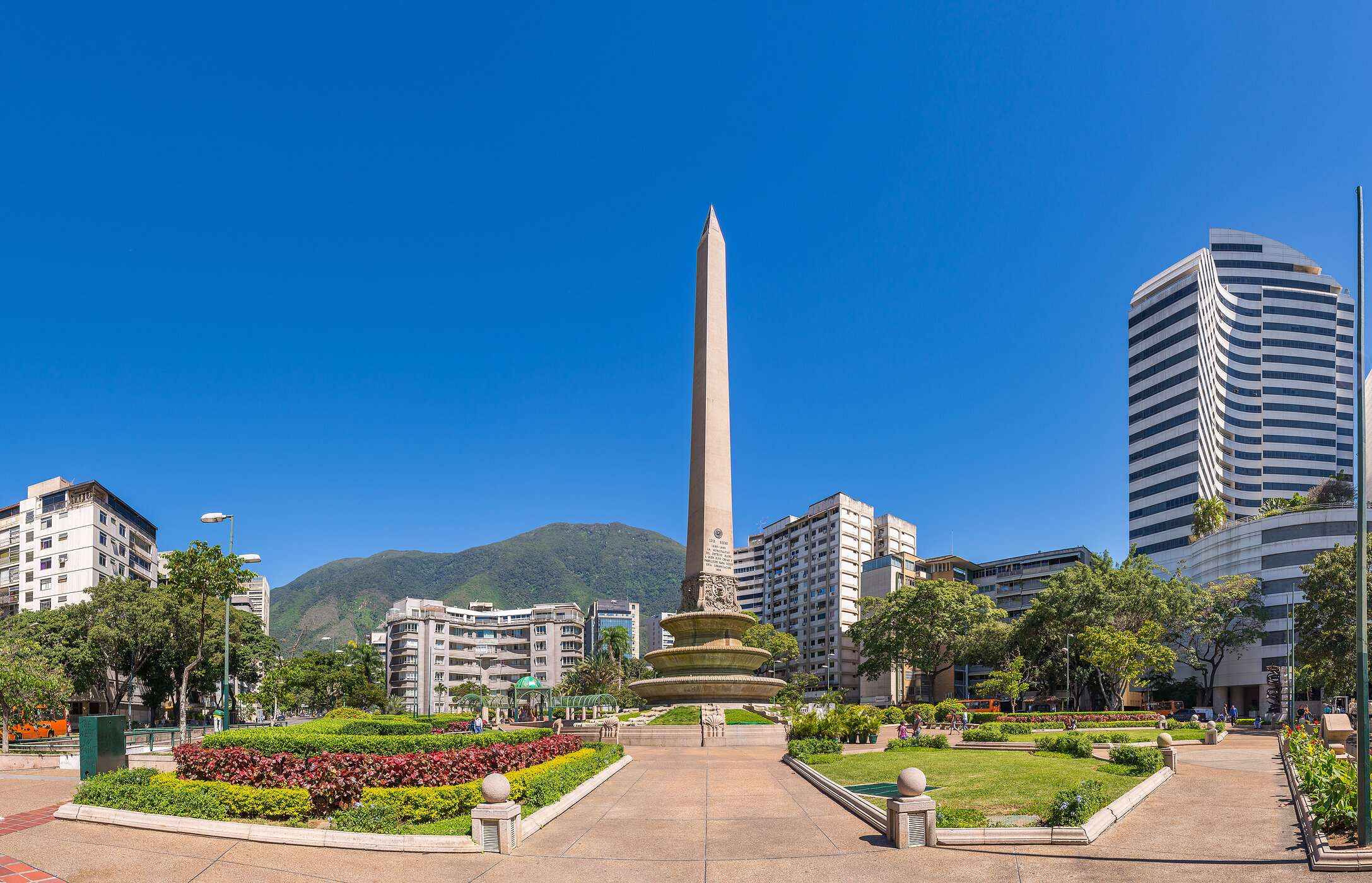 Obelisk-Monument, eine große Steinsäule inmitten eines Parks mit Blumen, umgeben von hohen Gebäuden in Venezuela.
