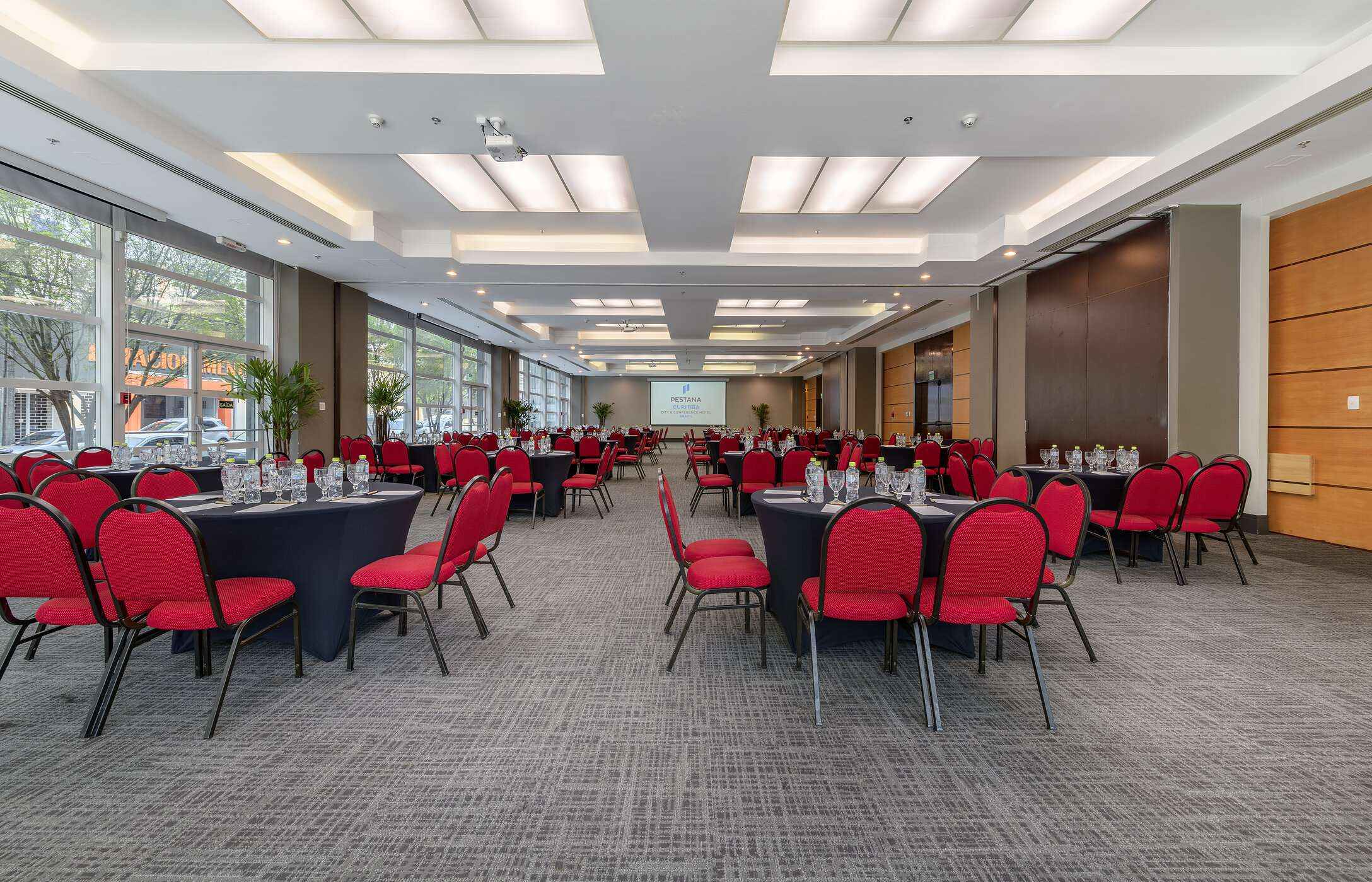 Raum für Meetings oder Konferenzen, mit mehreren runden Tischen, roten Stühlen, Gläsern und Wasserflaschen