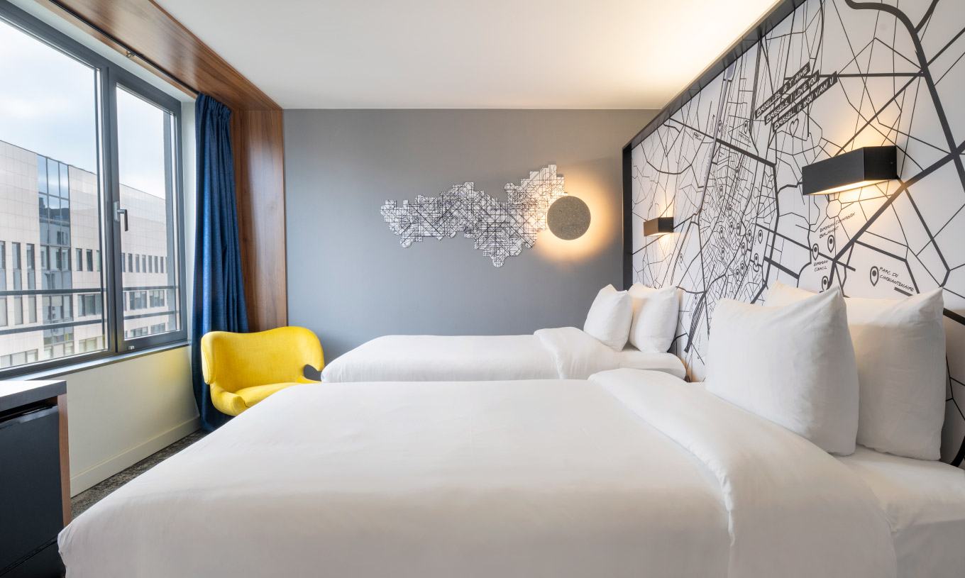 The Standard Twin at Pestana Brussels Schuman has two single beds, a yellow chair, and a window with a view