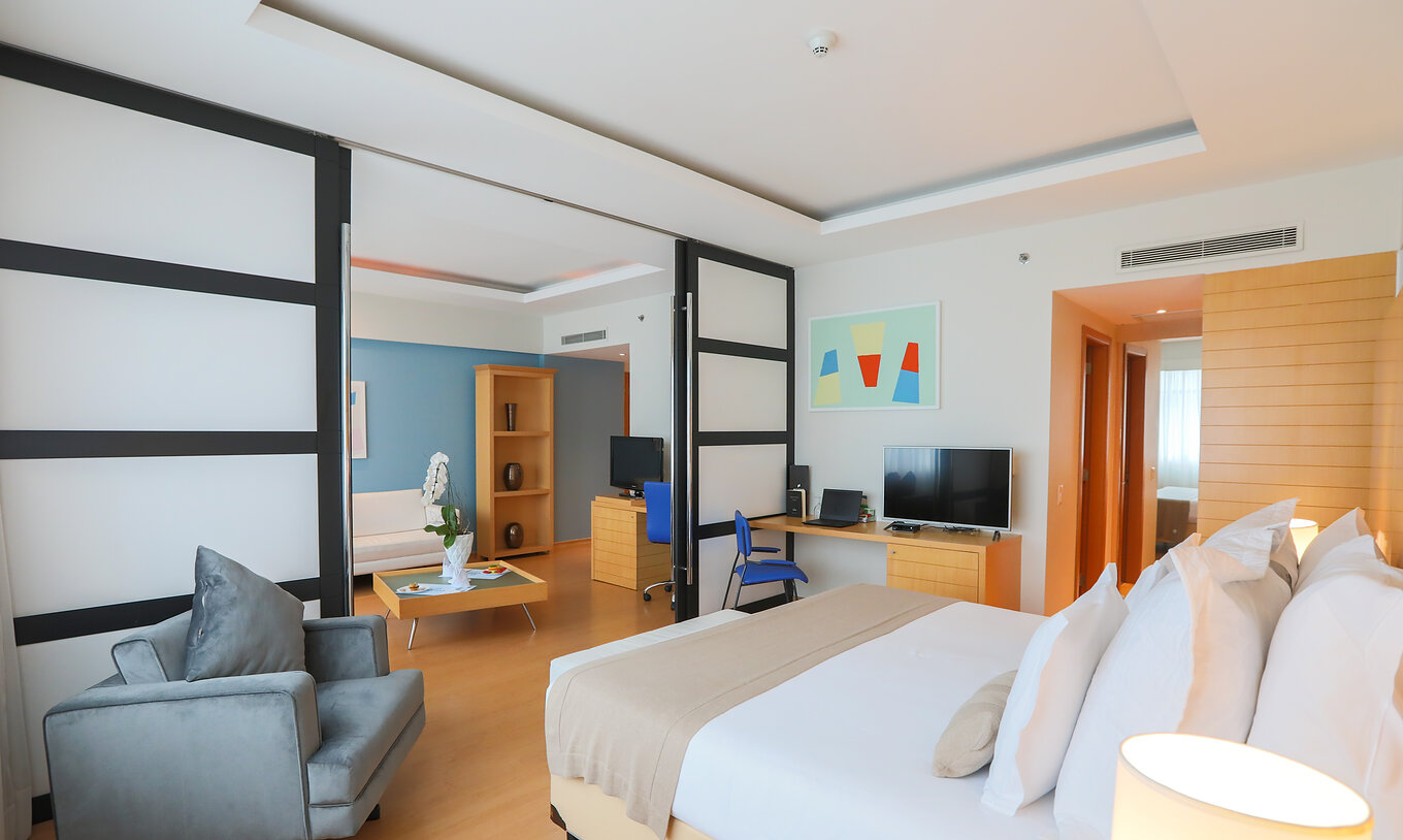 The Suite Master at Pestana Curitiba has a room with a king-size bed and a large living room with sofa and television
