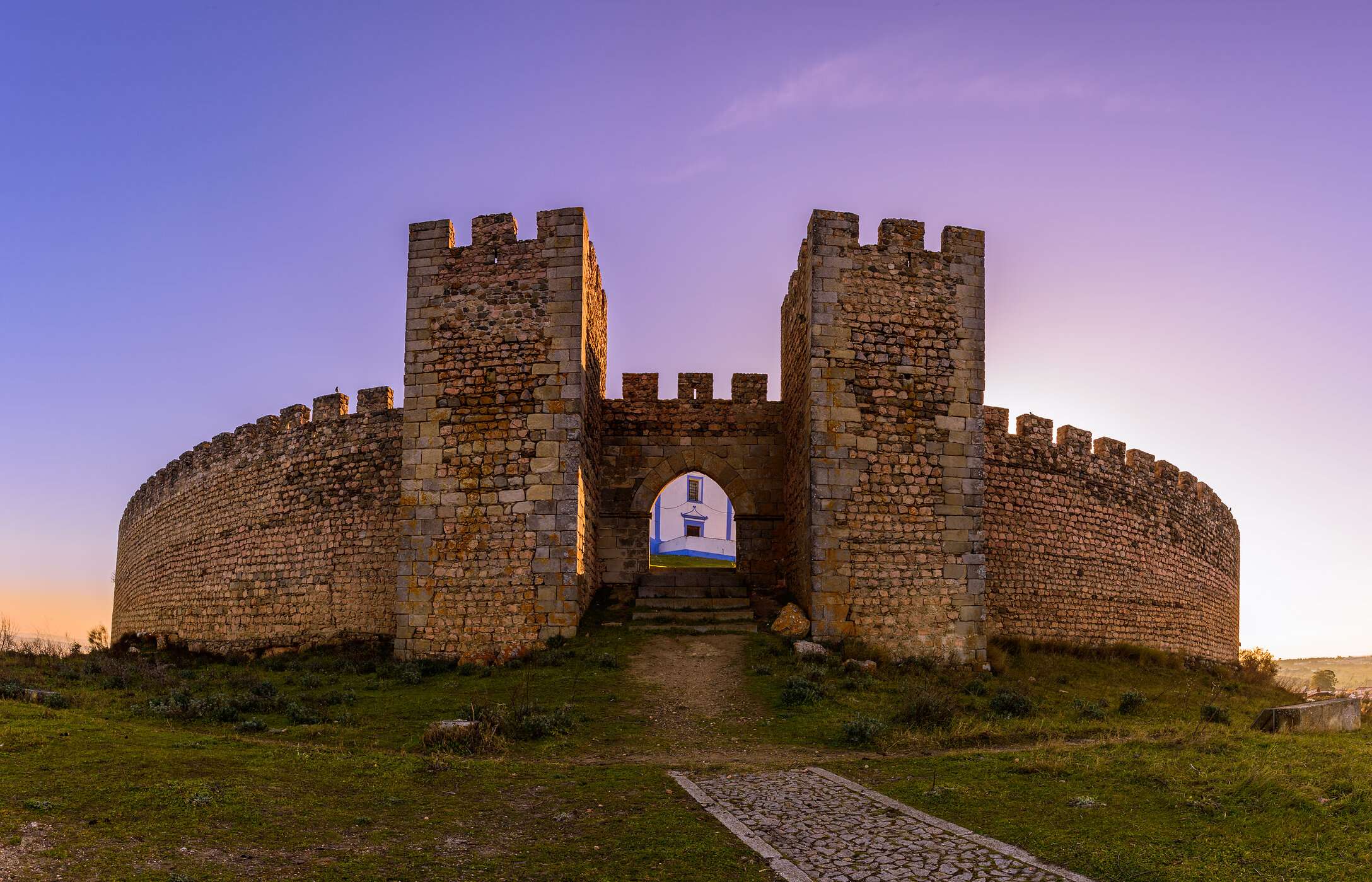 Imposing front view of the entrance to Arraiolos Castle, with stone walls and surrounding vegetation