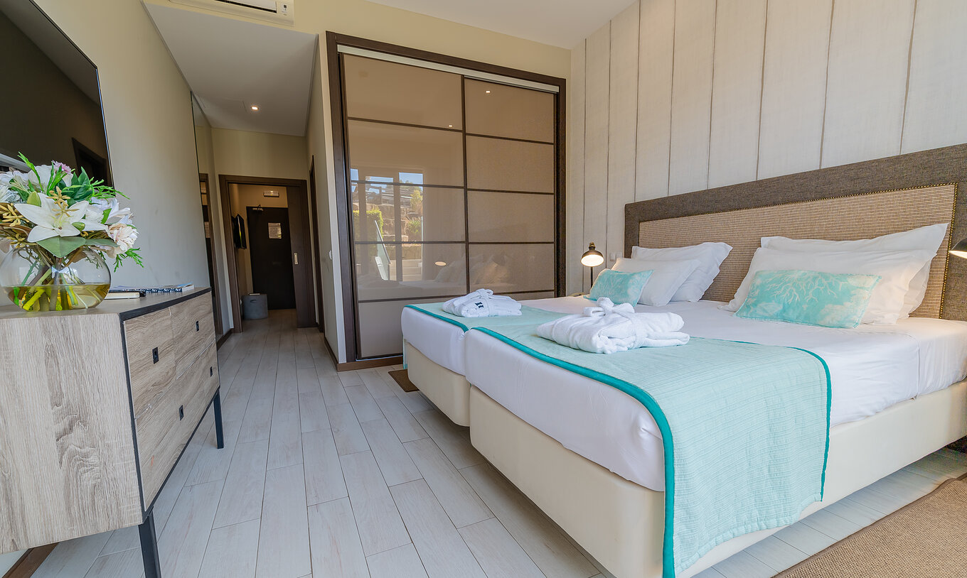 The Garden Suite at Pestana Alvor Park has two beds with a wooden dresser, a television, and a wardrobe with sliding doors