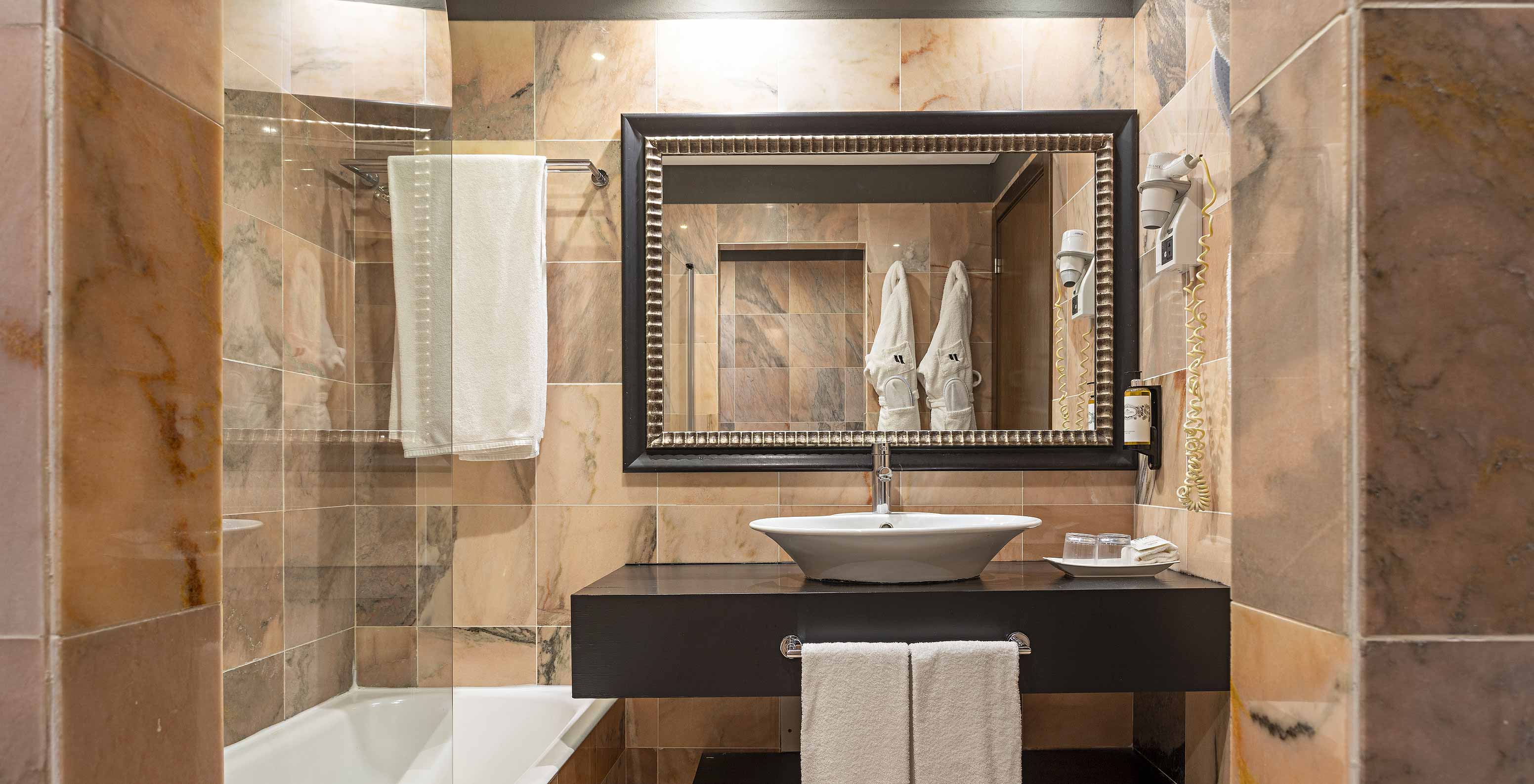 The Cliff Suite T1 at Pestana Alvor Praia has a bathroom with a bathtub, two bathrobes, and a hairdryer