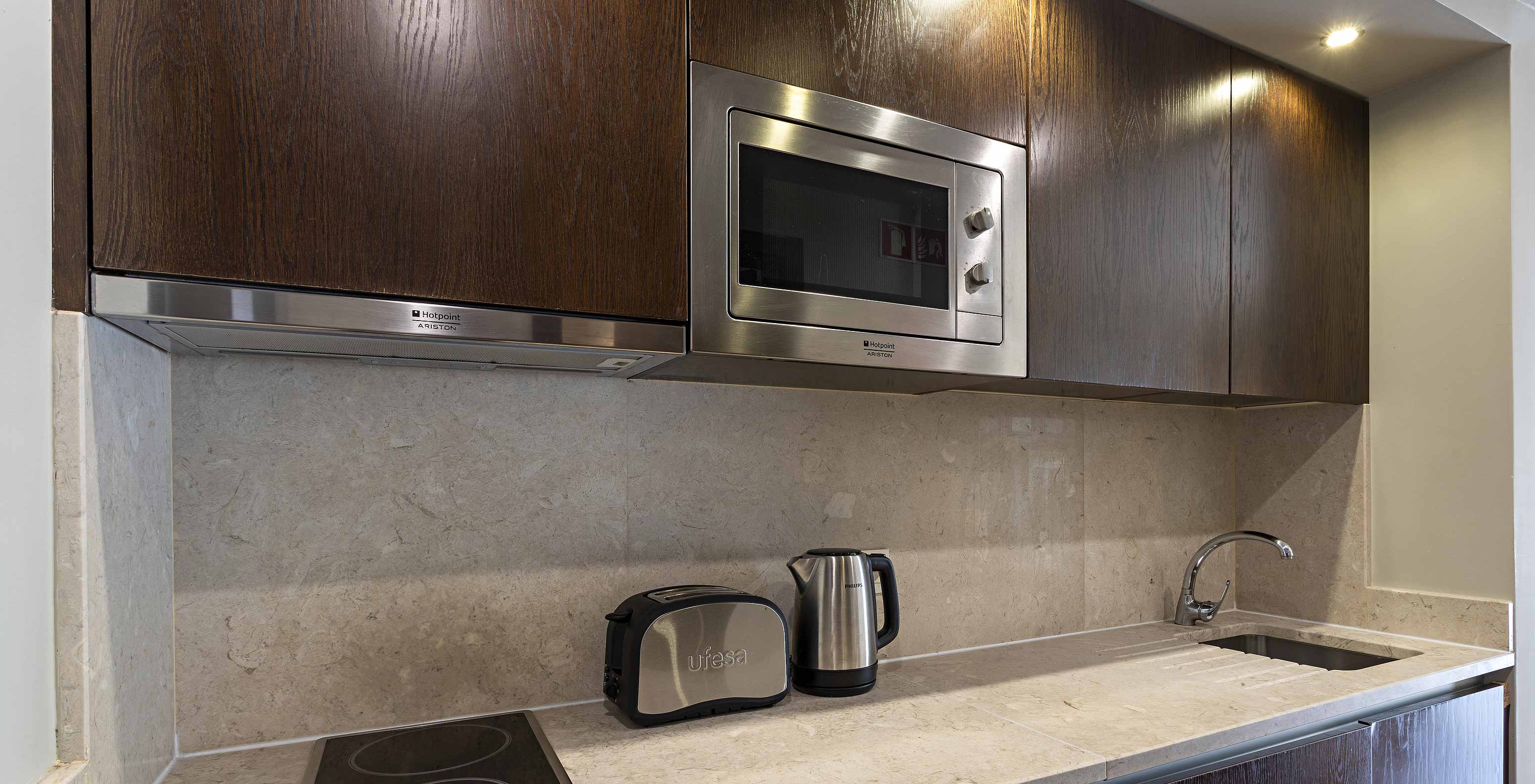 The Cliff Suite T1 at Pestana Alvor Praia has a dark wood kitchen and a stone counter, with a stove and a microwave
