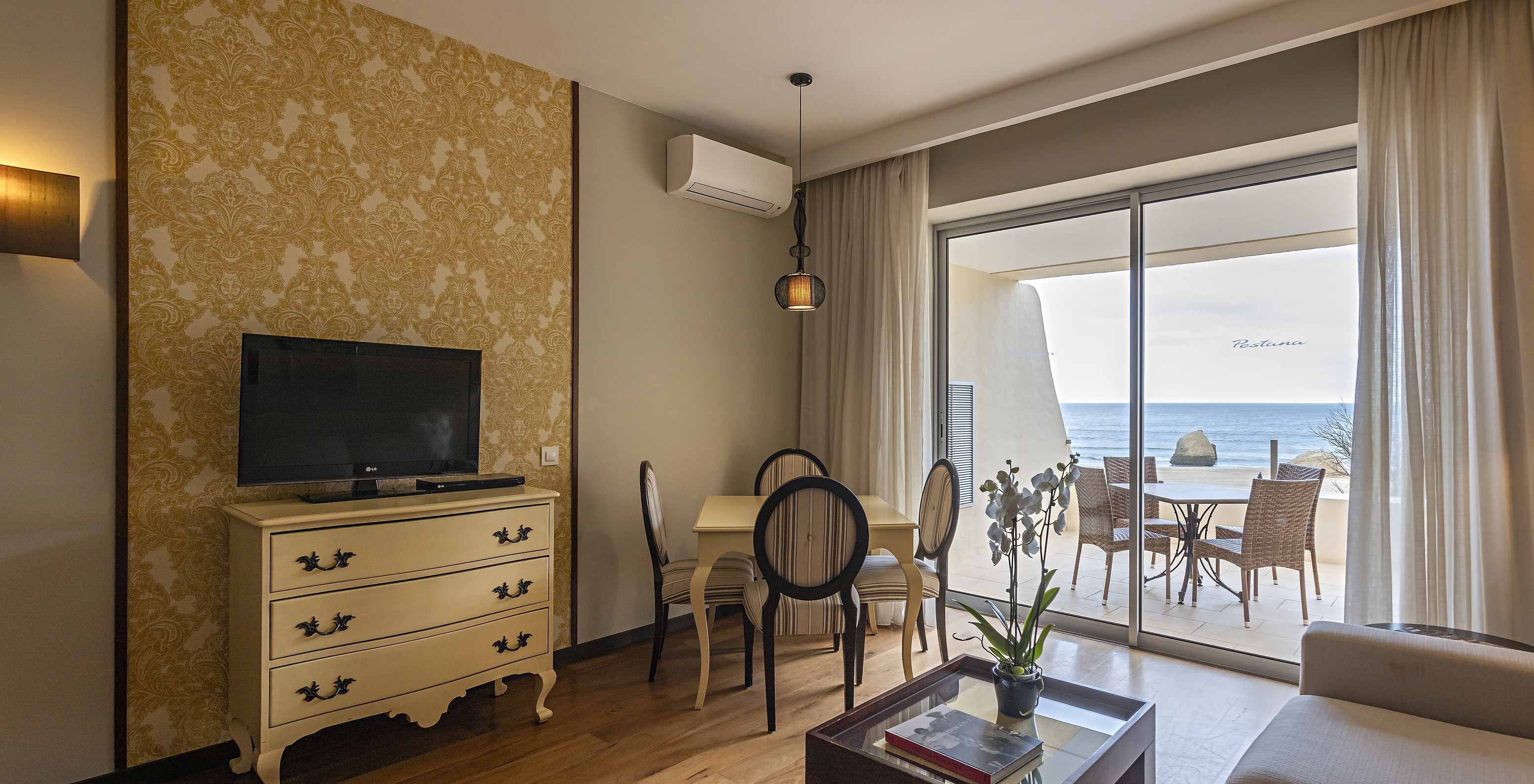 The Cliff Suite T1 at Pestana Alvor Praia has a living room with a TV and a balcony with a table, chairs, and a sea view