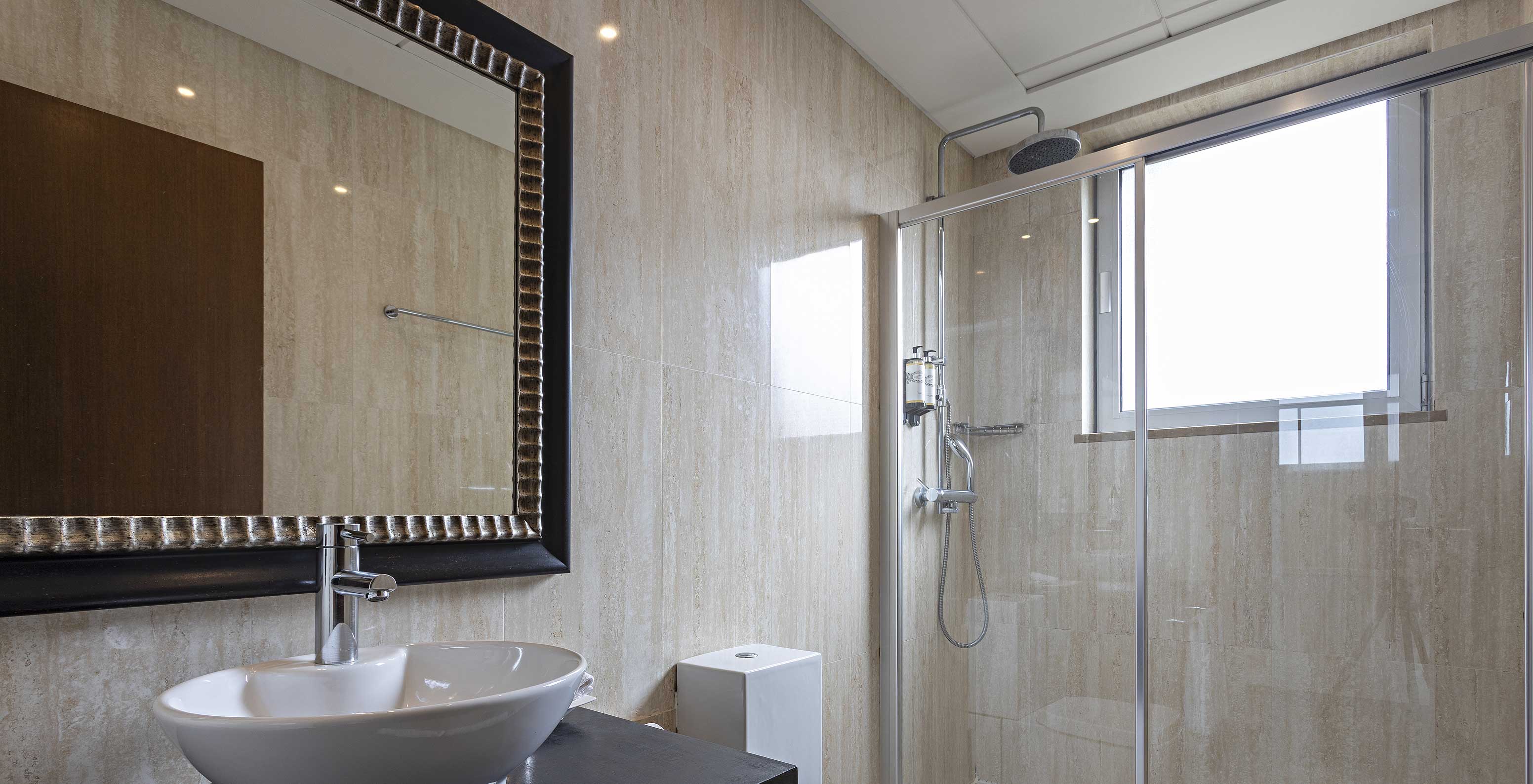 The Cliff Suite T2 at Pestana Alvor Praia has a modern bathroom with a window, a shower, a sink, and a mirror