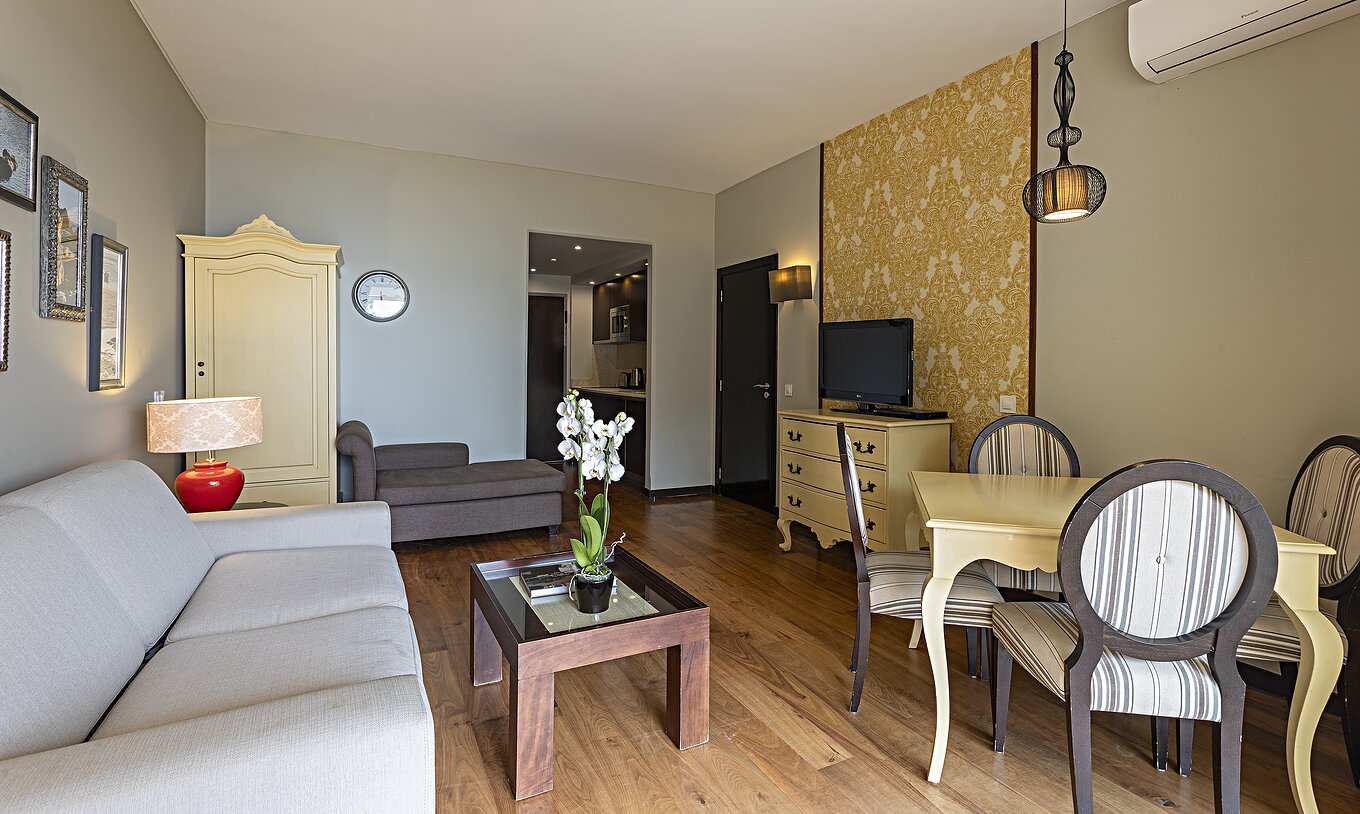The Cliff Suite T1 at Pestana Alvor Praia has a living room with a sofa, wallpaper, television, and a dining table