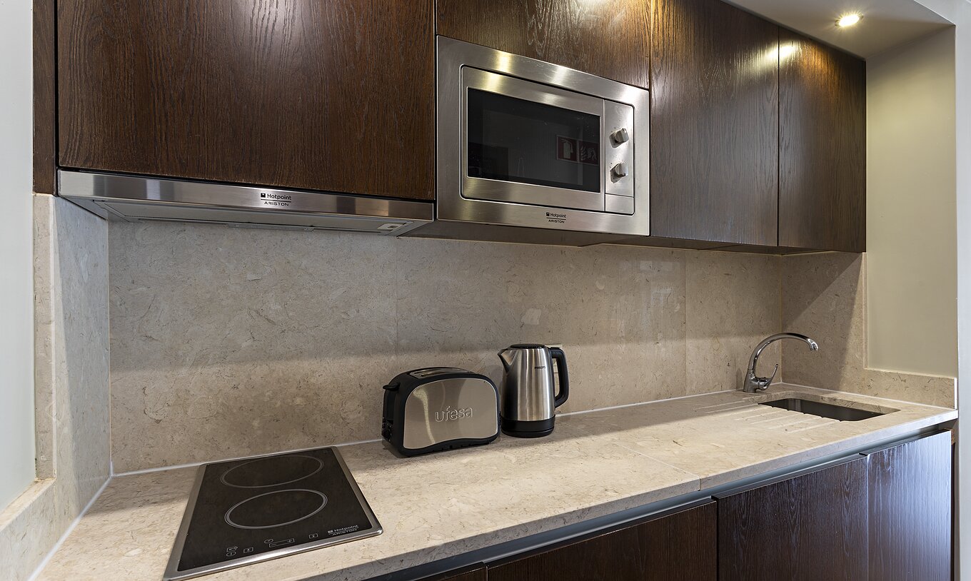 The Cliff Suite T1 at Pestana Alvor Praia has a dark wood kitchen and a stone counter, with a stove and a microwave