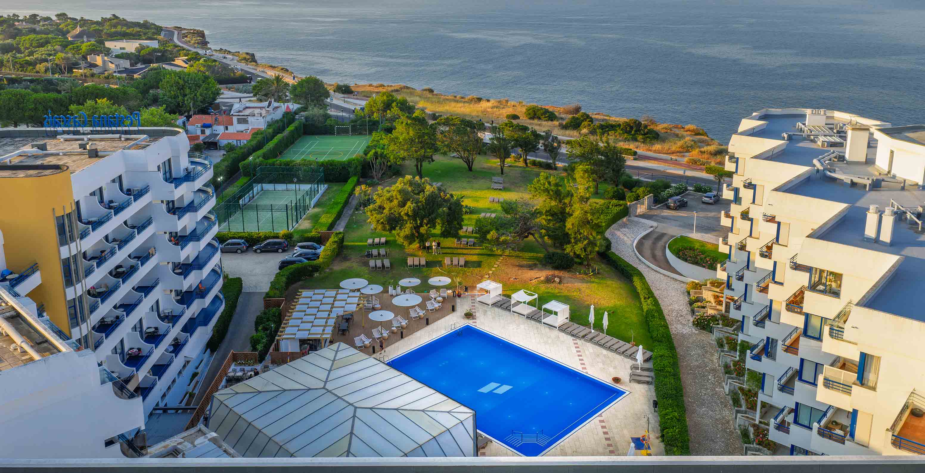 Aerial view of the hotel with the outdoor pool, gardens, and sea view