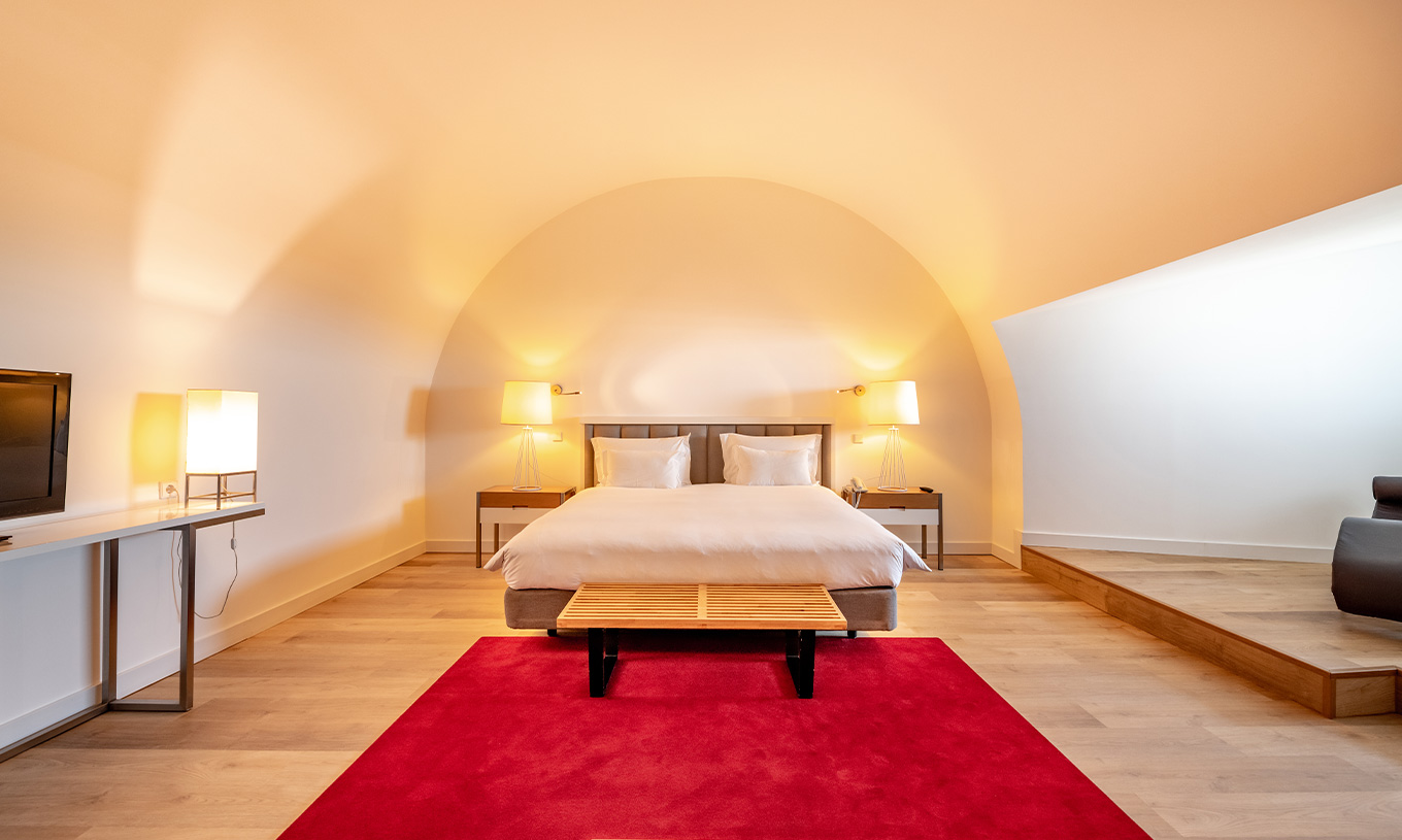 The Junior Family Suite at Pestana Cidadela Cascais has a double bed with a bench at the foot and a red carpet