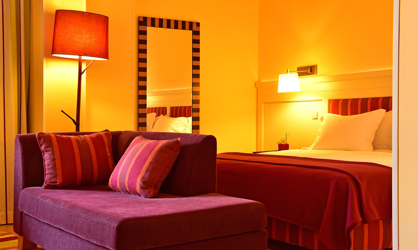 The Junior Suite of Pestana Sintra Golf has a double bed, a mirror on the wall, and a small red sofa