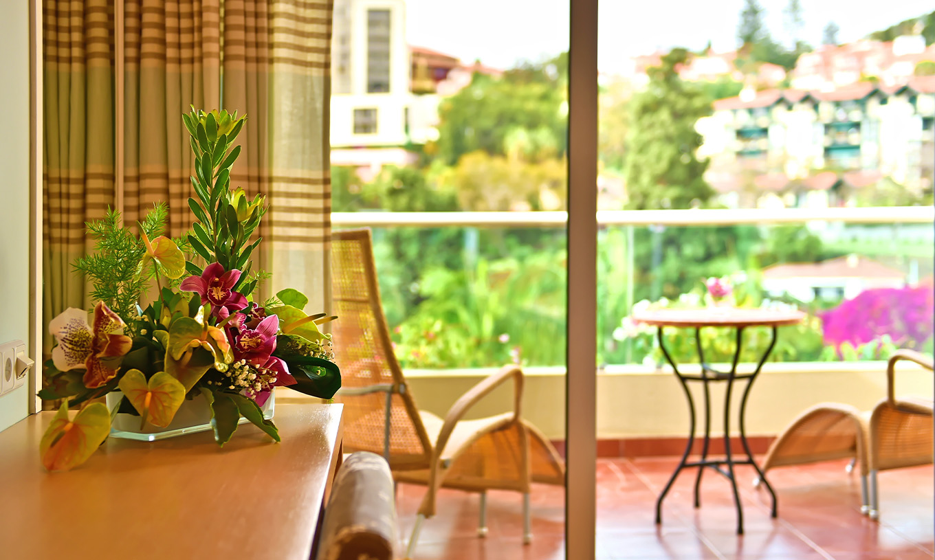 The Classic Double Room with Pool View at Pestana Carlton Madeira has a dresser with flowers and a balcony with a table