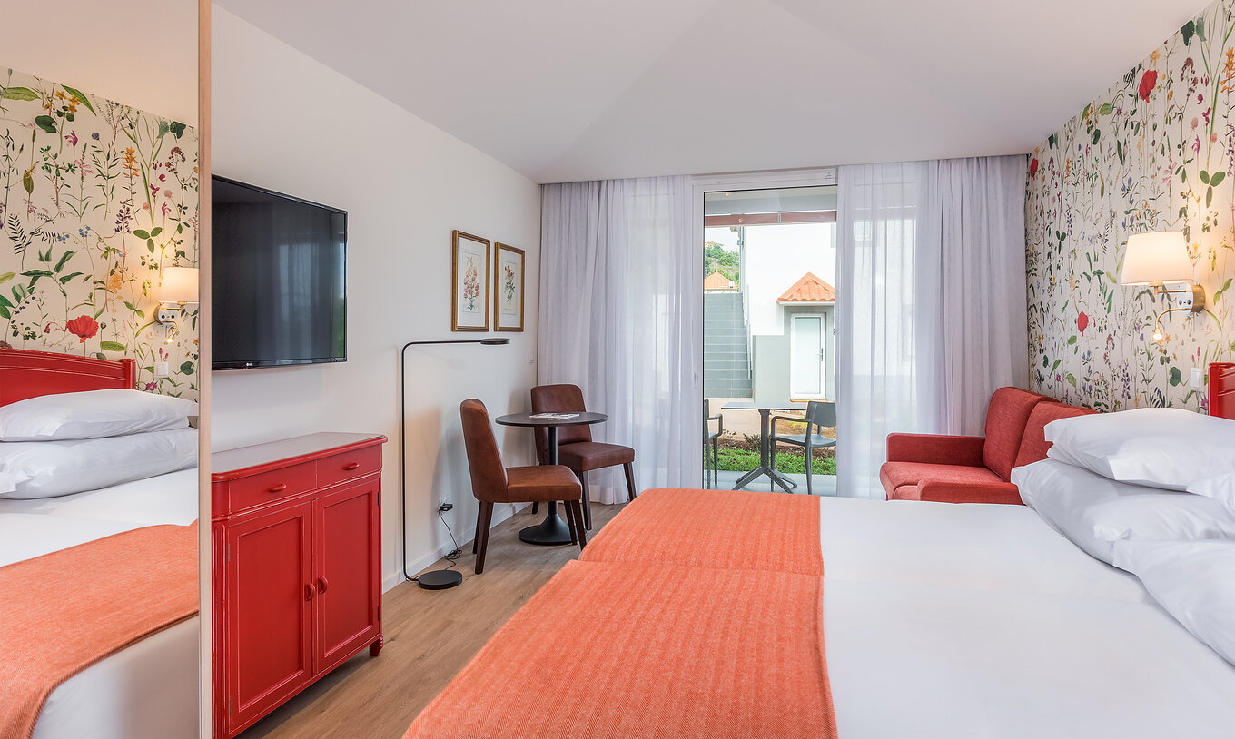 The Sea View Studio of Pestana Quinta do Arco has two joined beds, television, red sofa, and balcony with table and chairs