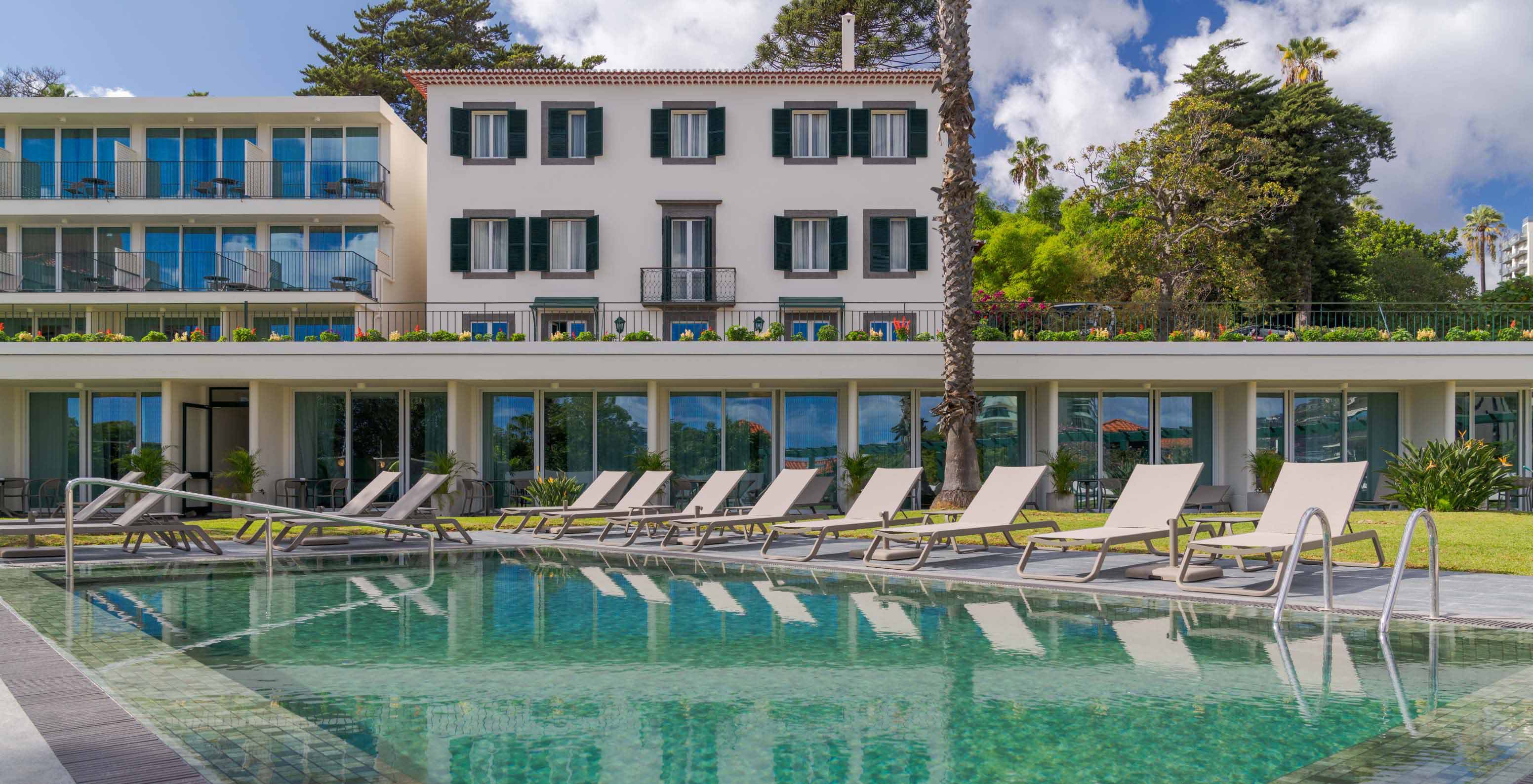 View of the outdoor pool at Pestana Quinta Perestrello, a Charming Hotel in Madeira, with the building behind