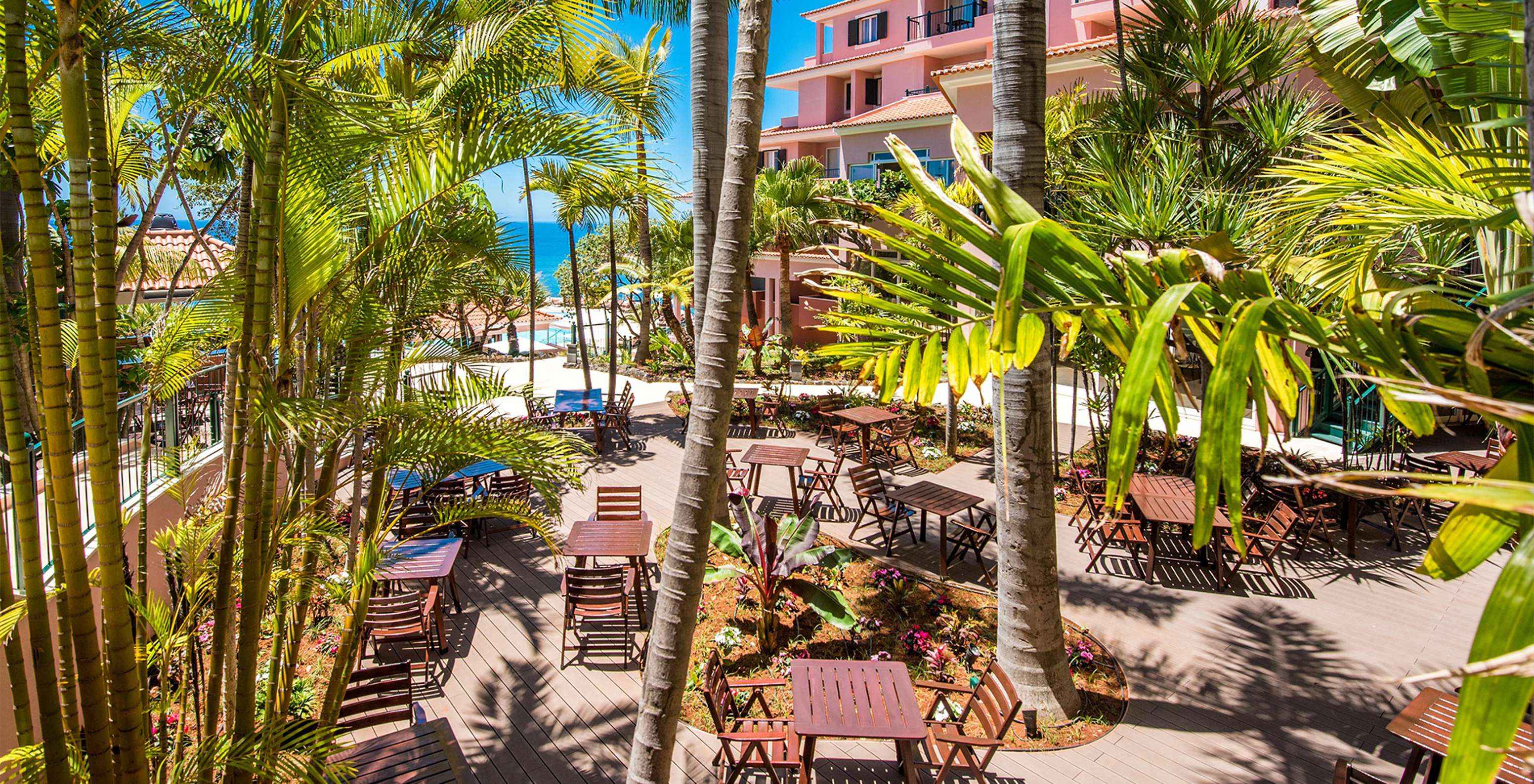 Pestana Royal All Inclusive, hotel near the beach, has a garden with palm trees, chairs, and tables